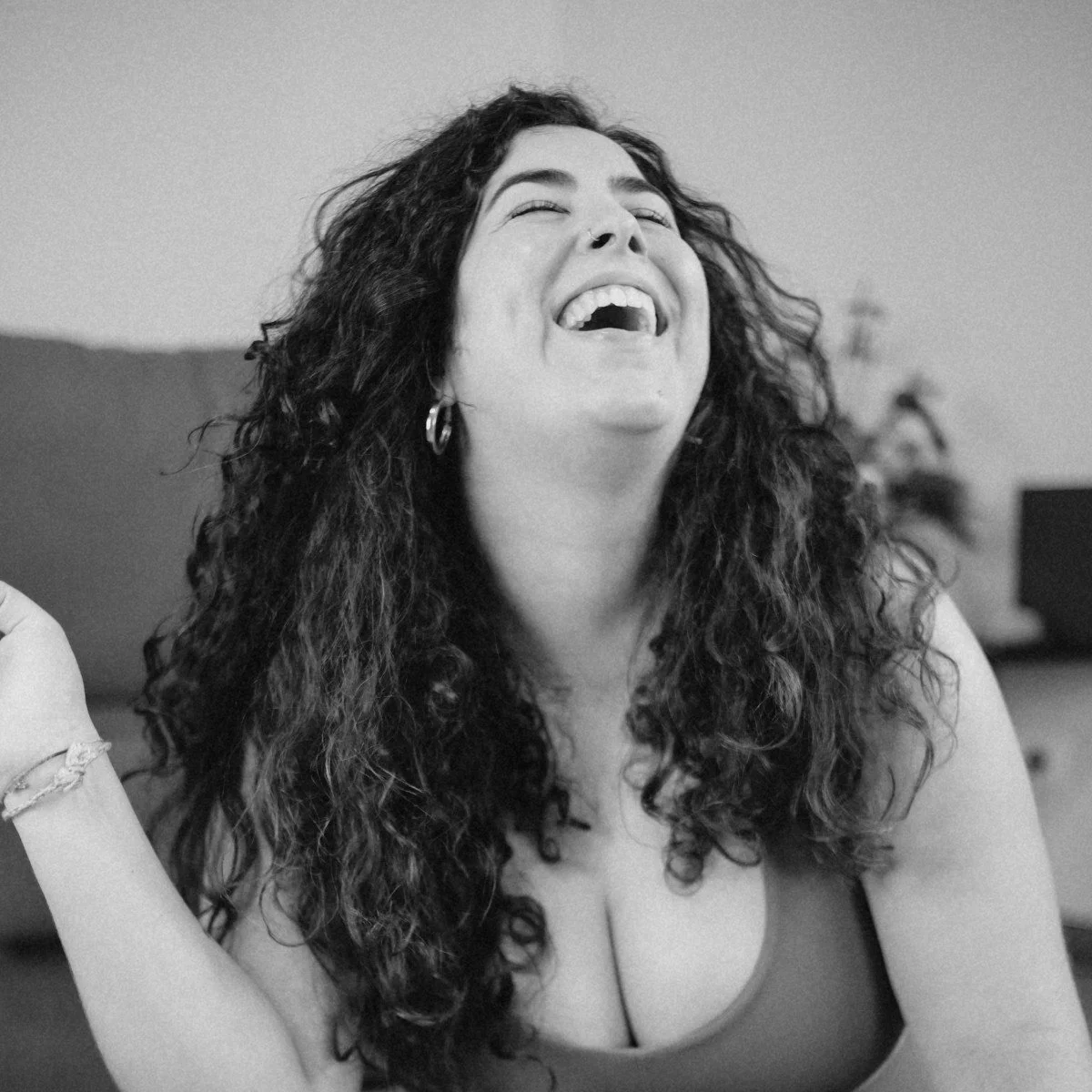 Woman with long curly hair laughing, wearing hoop earrings, in a casual setting.