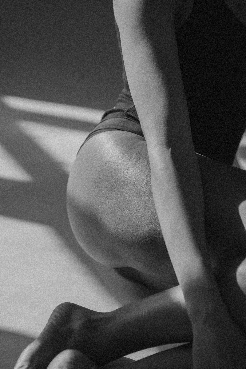 Close-up black and white photo of a person doing a leg exercise, focusing on their lower body, with a gym equipment in the background.