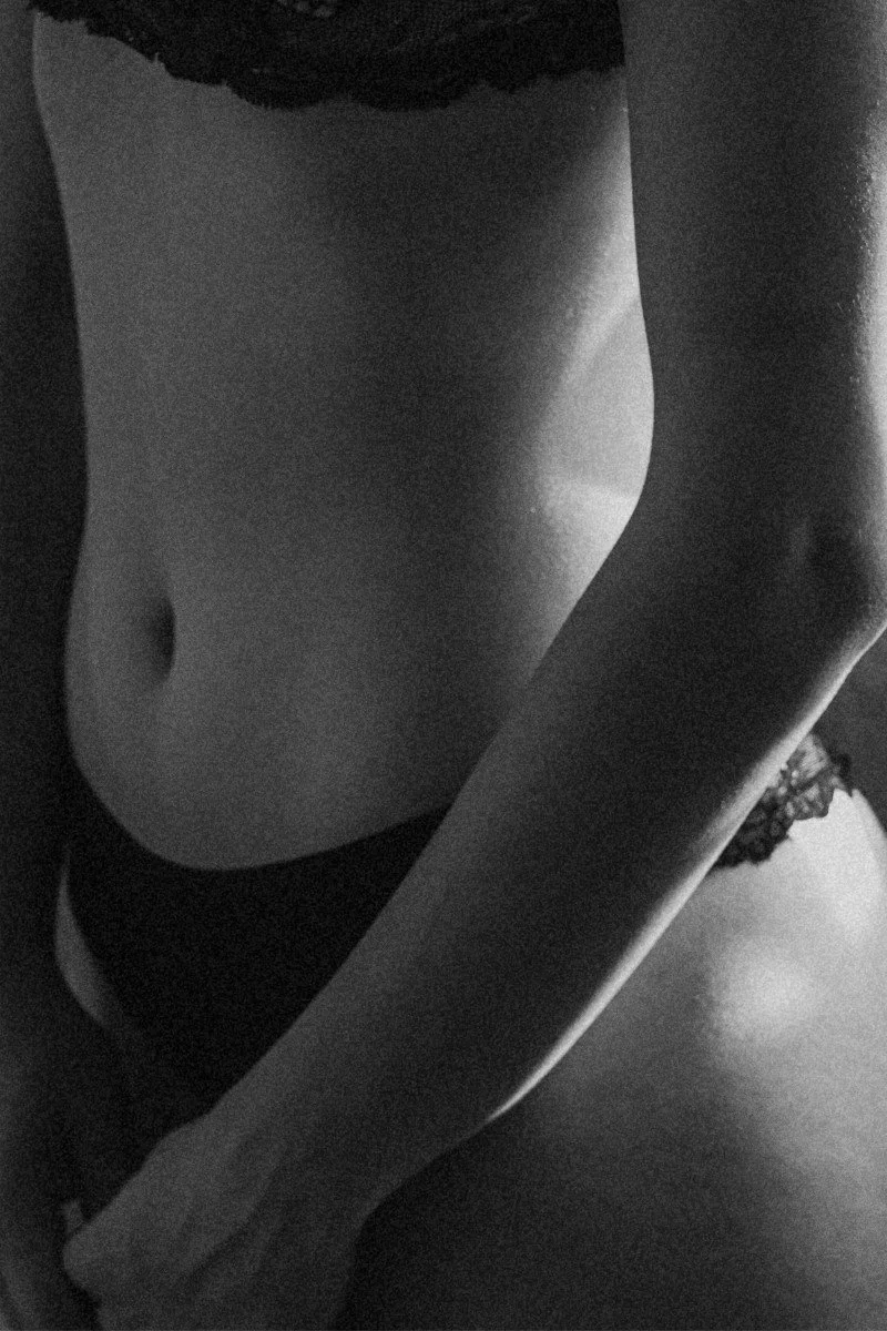 Close-up black and white photo of a woman's toned abdomen, including her navel, with part of her arm and hip visible.