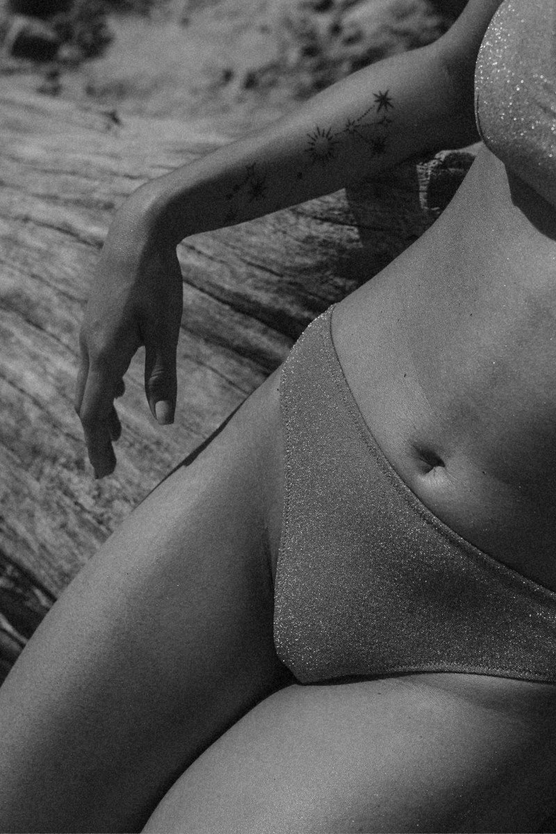 Close-up of a woman's midsection, showing her arm with a star tattoo, and wearing glittery underwear.