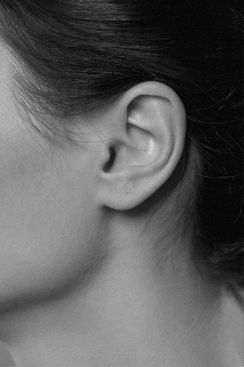 Close-up black and white photo of a woman's ear with dark hair partially covering it.