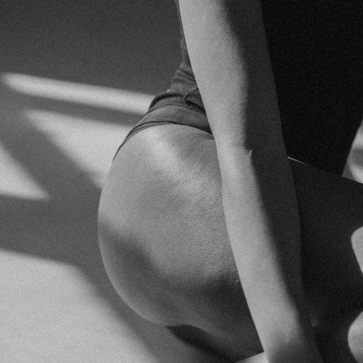 Close-up of a person's leg and back in black and white, with a portion of the body obscured by a piece of furniture or structure.