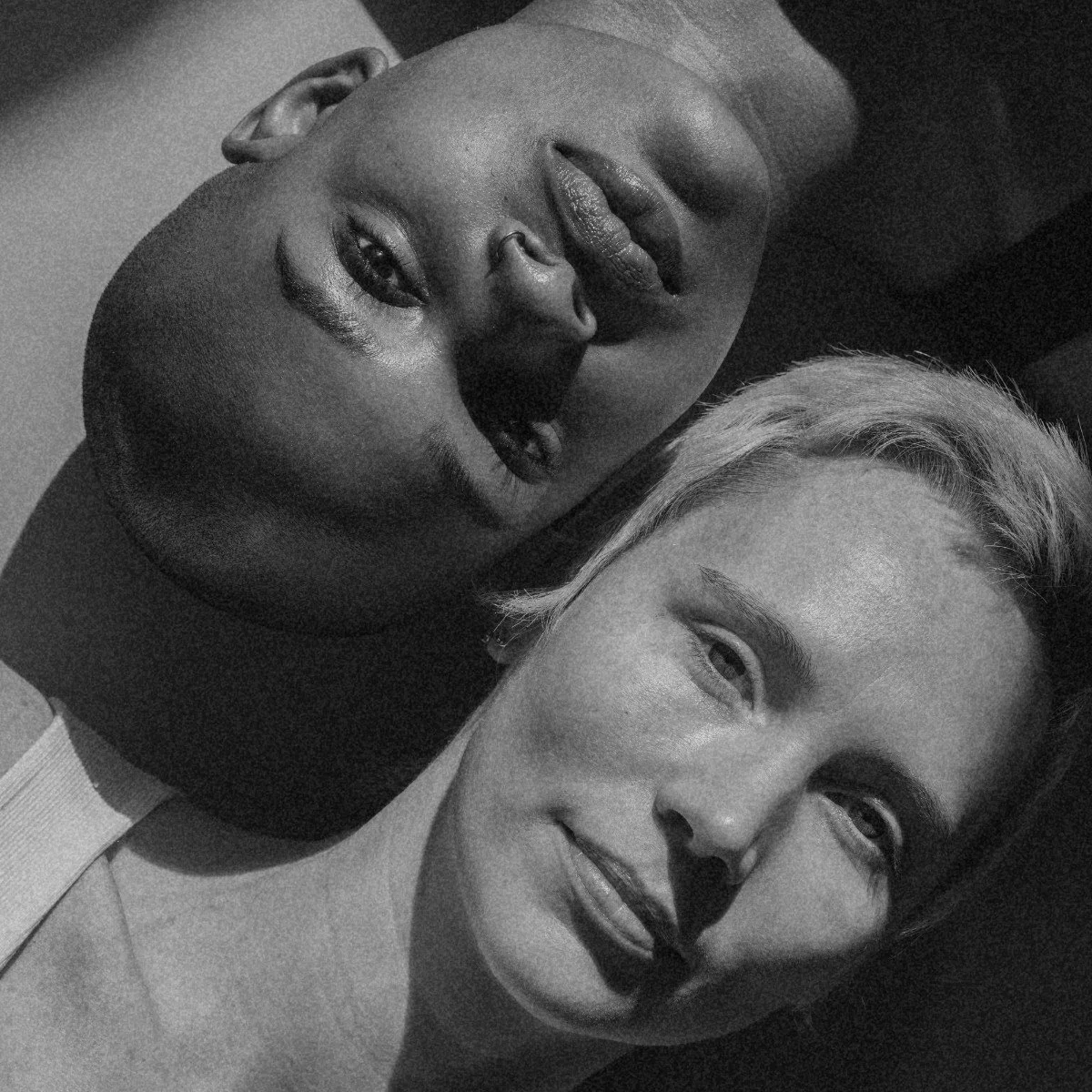 Black and white photo of two people lying down with heads touching and smiling at the camera.