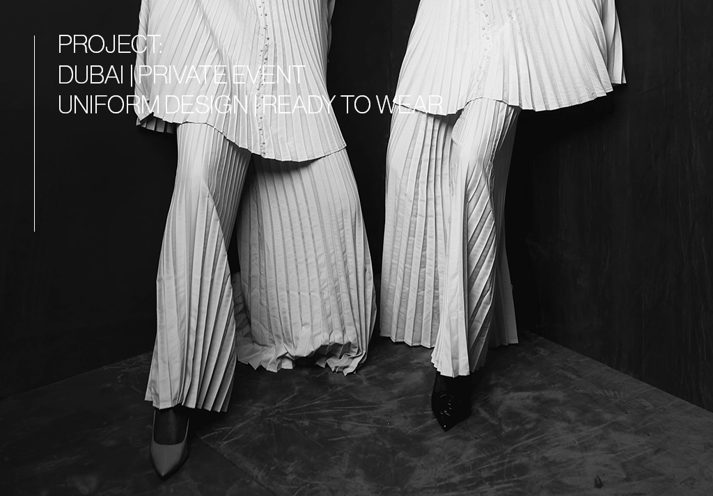 Two models wearing pleated wide-leg garments in a fashion display, with text overlay about a project and event in Dubai featuring a uniform design.