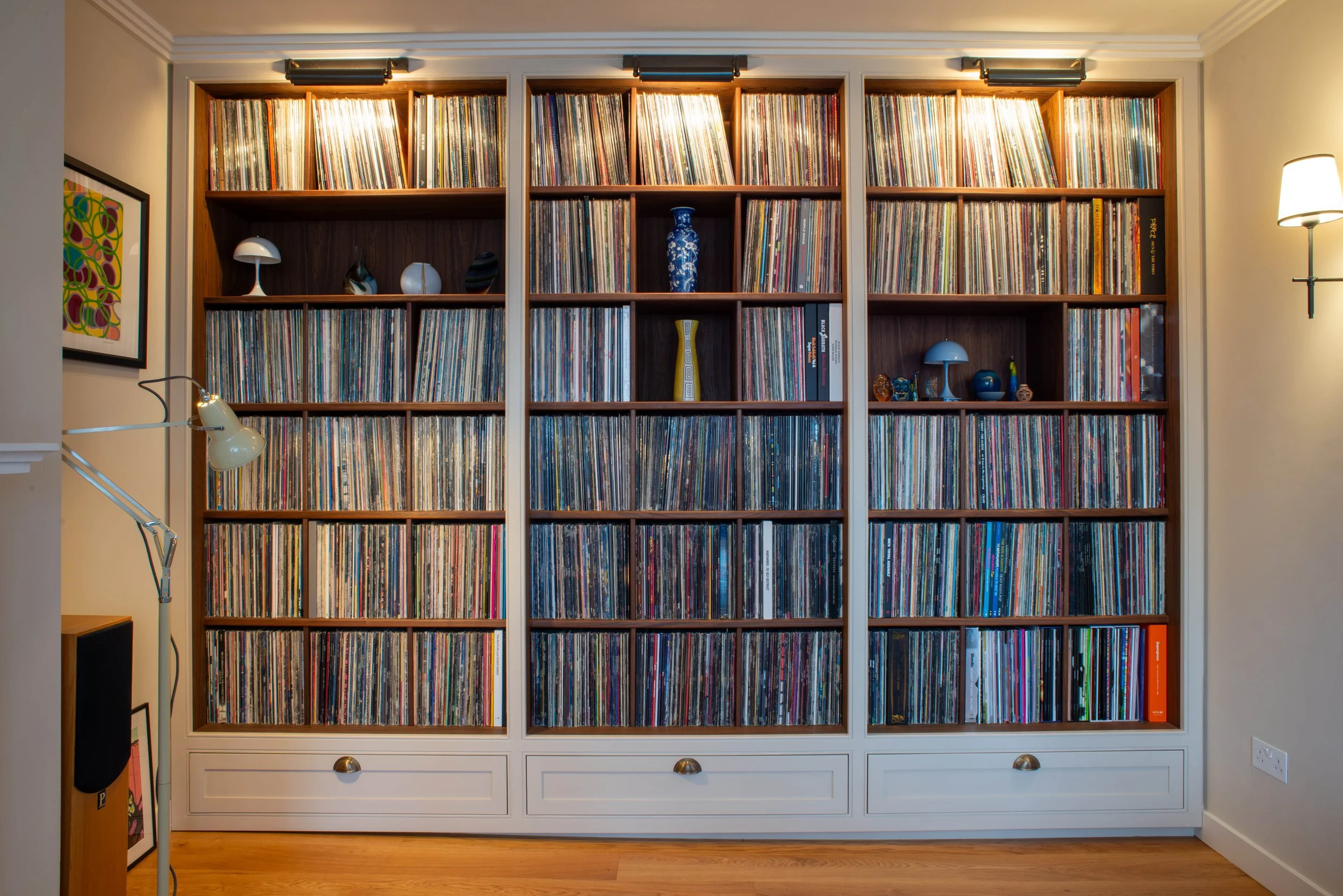 Empty wooden bookshelves with compartments and two lower drawers on a wall, featuring light brown wood and white trim, with overhead lighting.