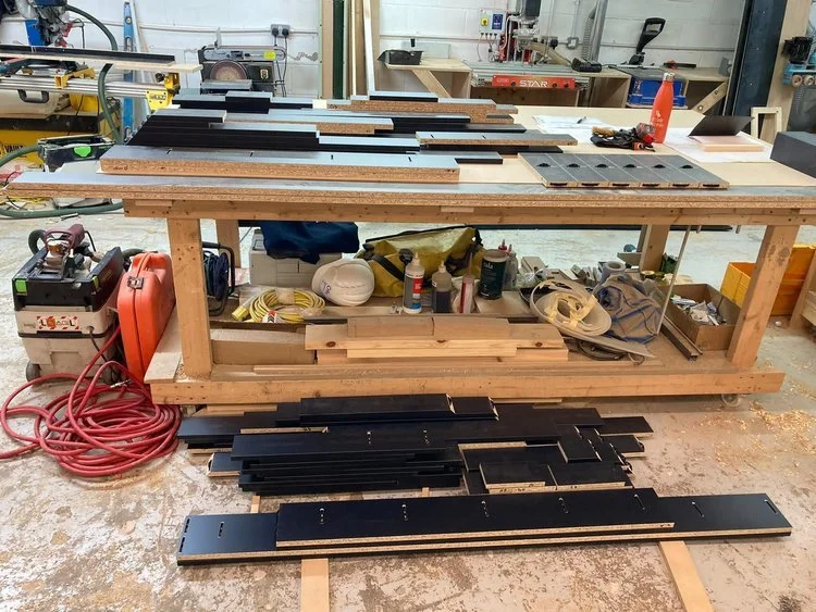 Woodworking workshop with workbench, stacked wooden planks, tools, and equipment.