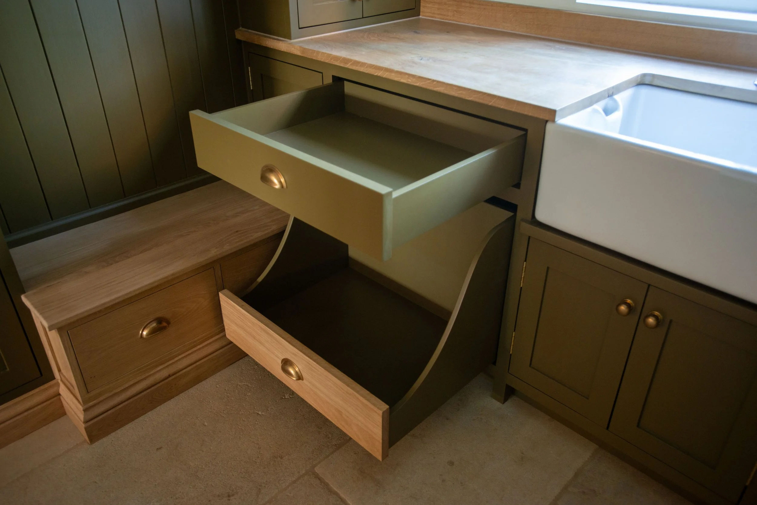 Empty wooden bookshelf with square compartments and bottom drawers, illuminated by a wall-mounted lamp in a room with light-colored walls and hardwood floor.