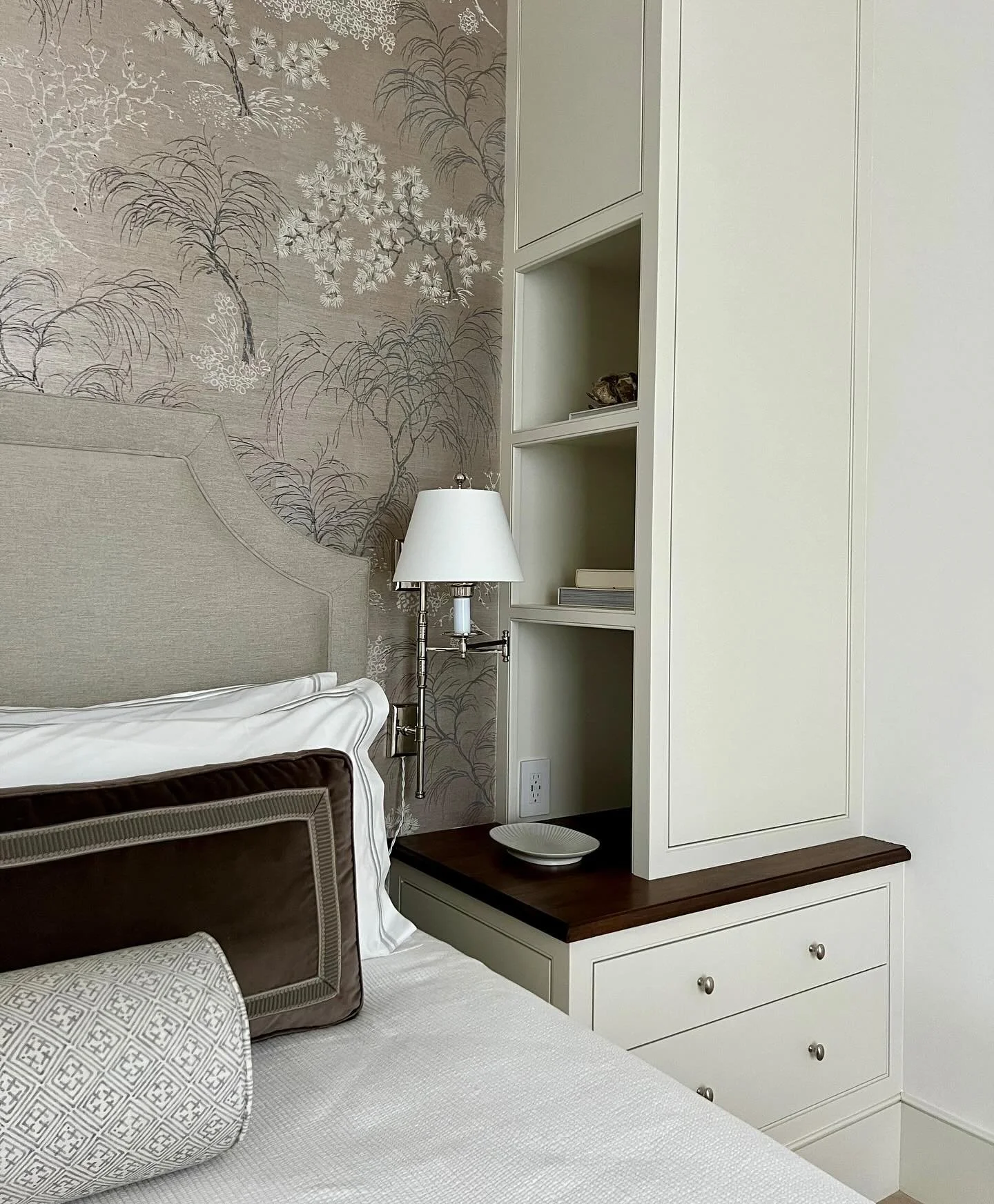 View of the main bedroom suite at #dfi_kiawahcottage. Custom painted cabinetry with a walnut countertop accent surrounds the bed to create a cozy alcove and also provides bedside storage. Fabrics for custom pillows were thoughtfully selected to coord
