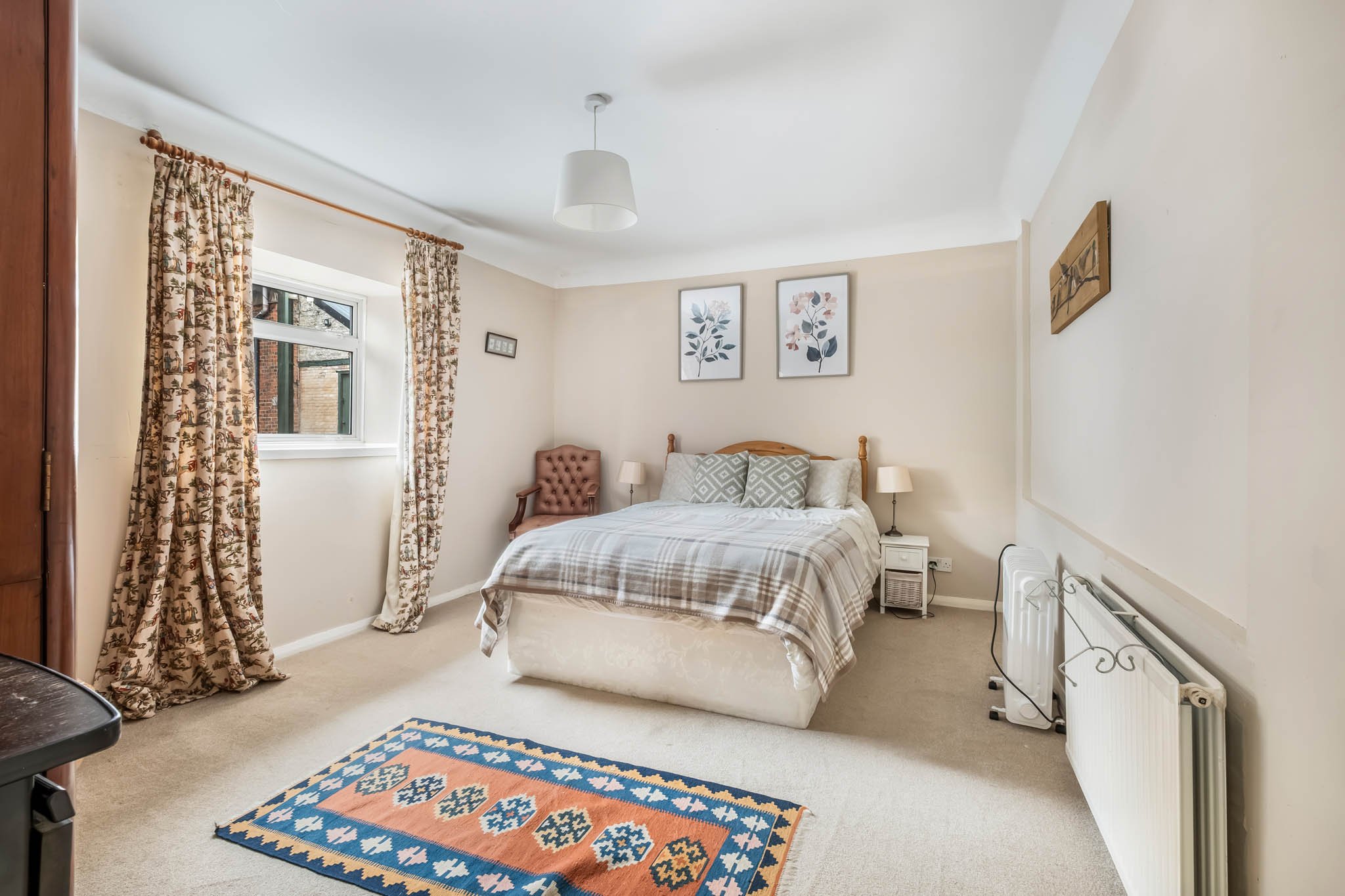 A bedroom with a bed, two lamps, wall art, a window with curtains, and a carpet.