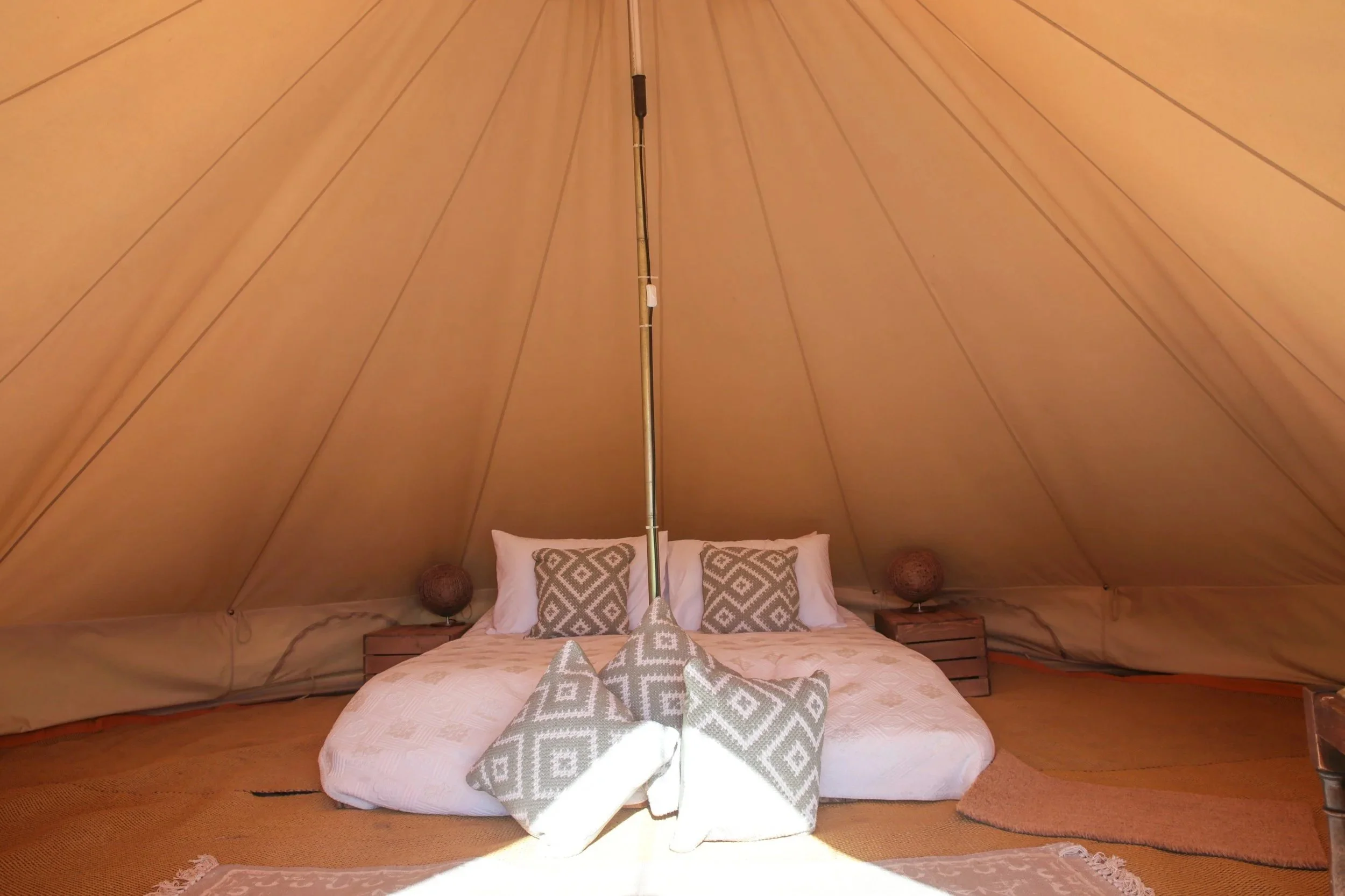 Interior view of a cozy tent with a bed, pillows, and decorative lamps on side tables.
