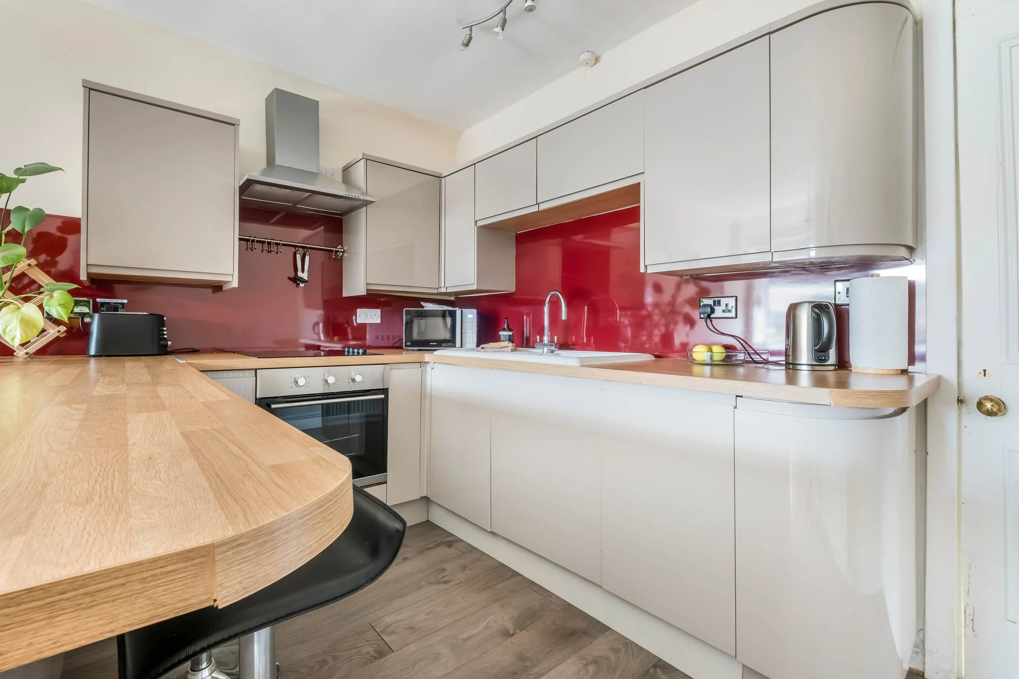 Modern kitchen with white cabinetry, red backsplash, wooden countertop, and appliances including microwave, toaster, kettle, and oven.