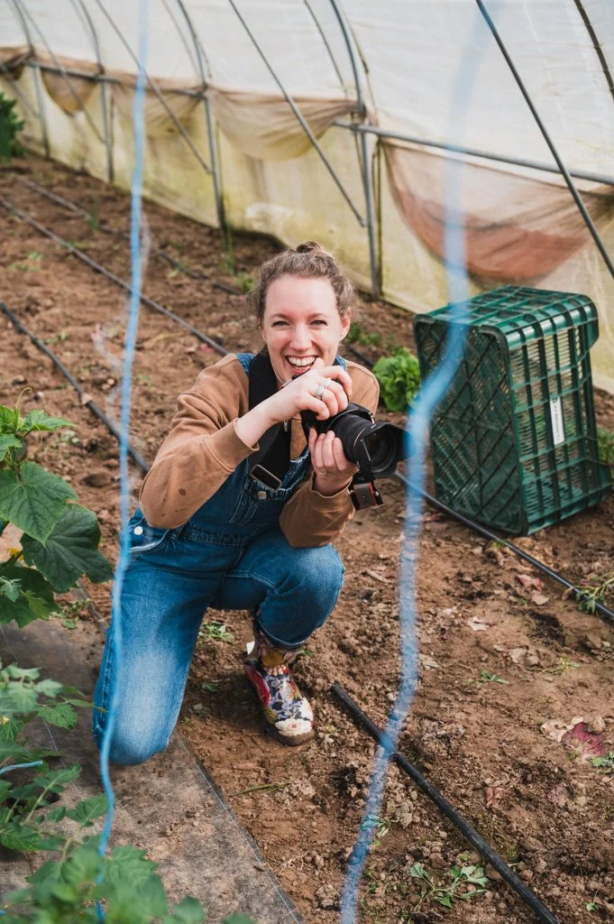 Marijke lacht, geknield in serre met camera in de hand