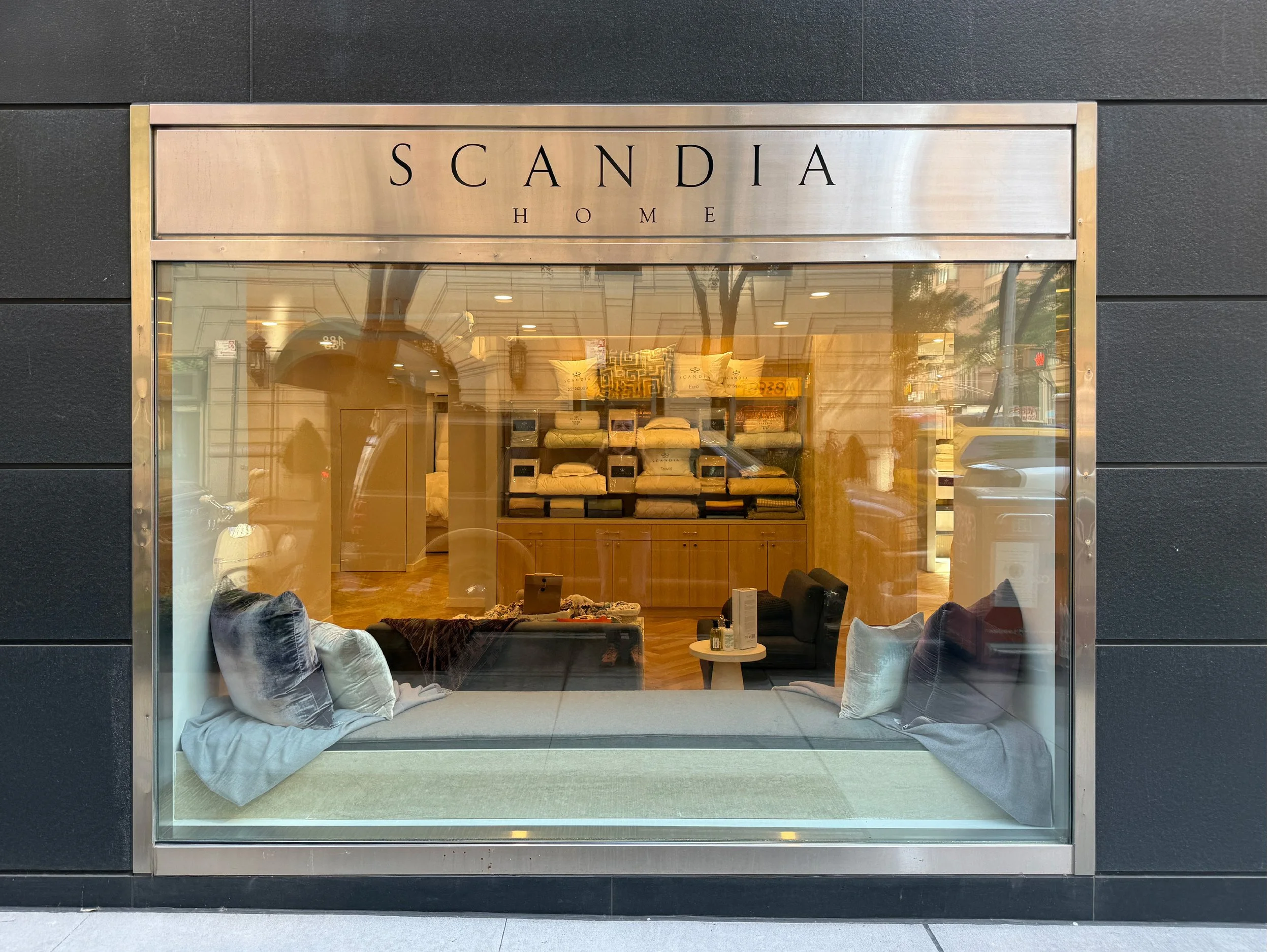 Storefront window display for Scandia Home, showcasing pillows and bedding inside.