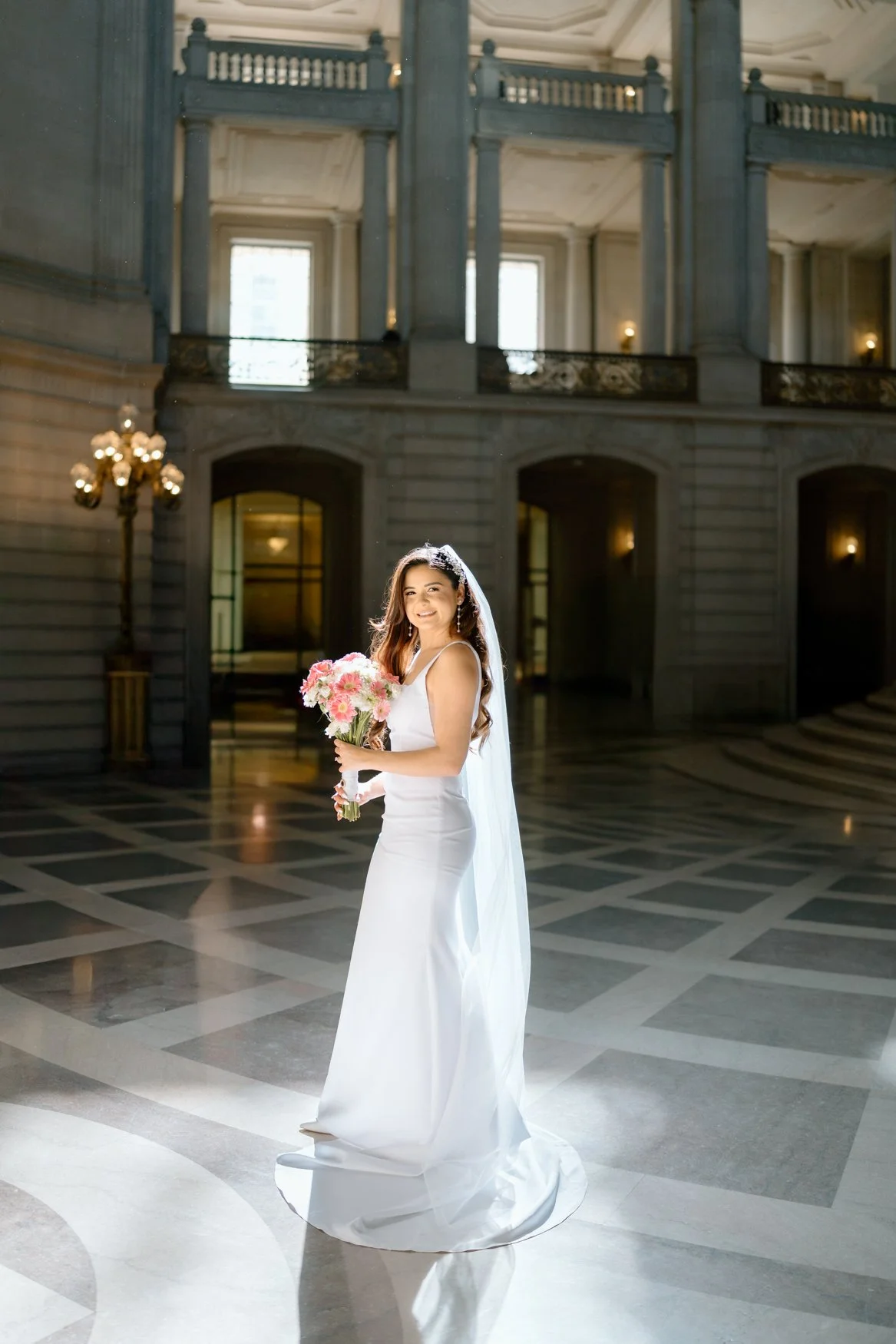 Solo of bride with dramatic sunlight spilling through San Francisco City Hall's windows, by By Evening Photography, destination elopement photographer