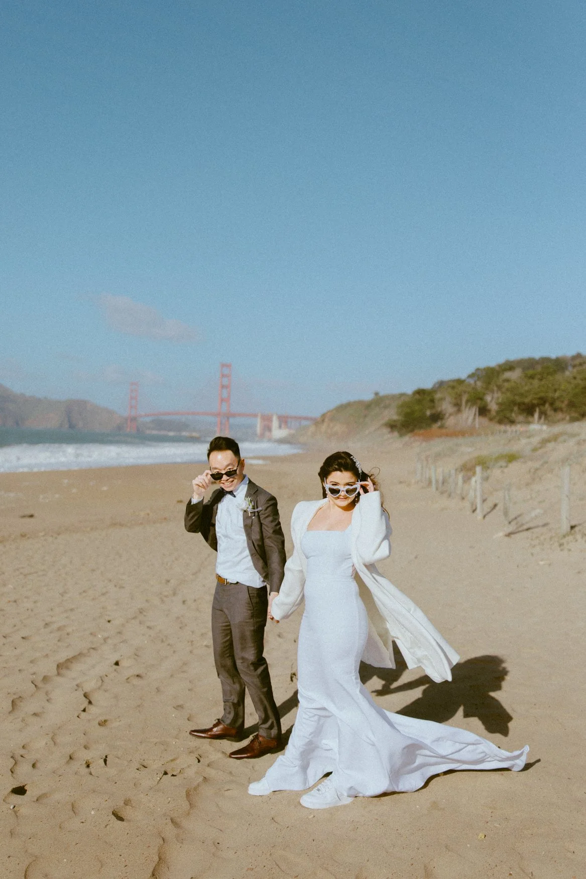 Cute wedding photos of Carla and Jonathan playing with their bride and groom sunglasses in Baker Beach, california