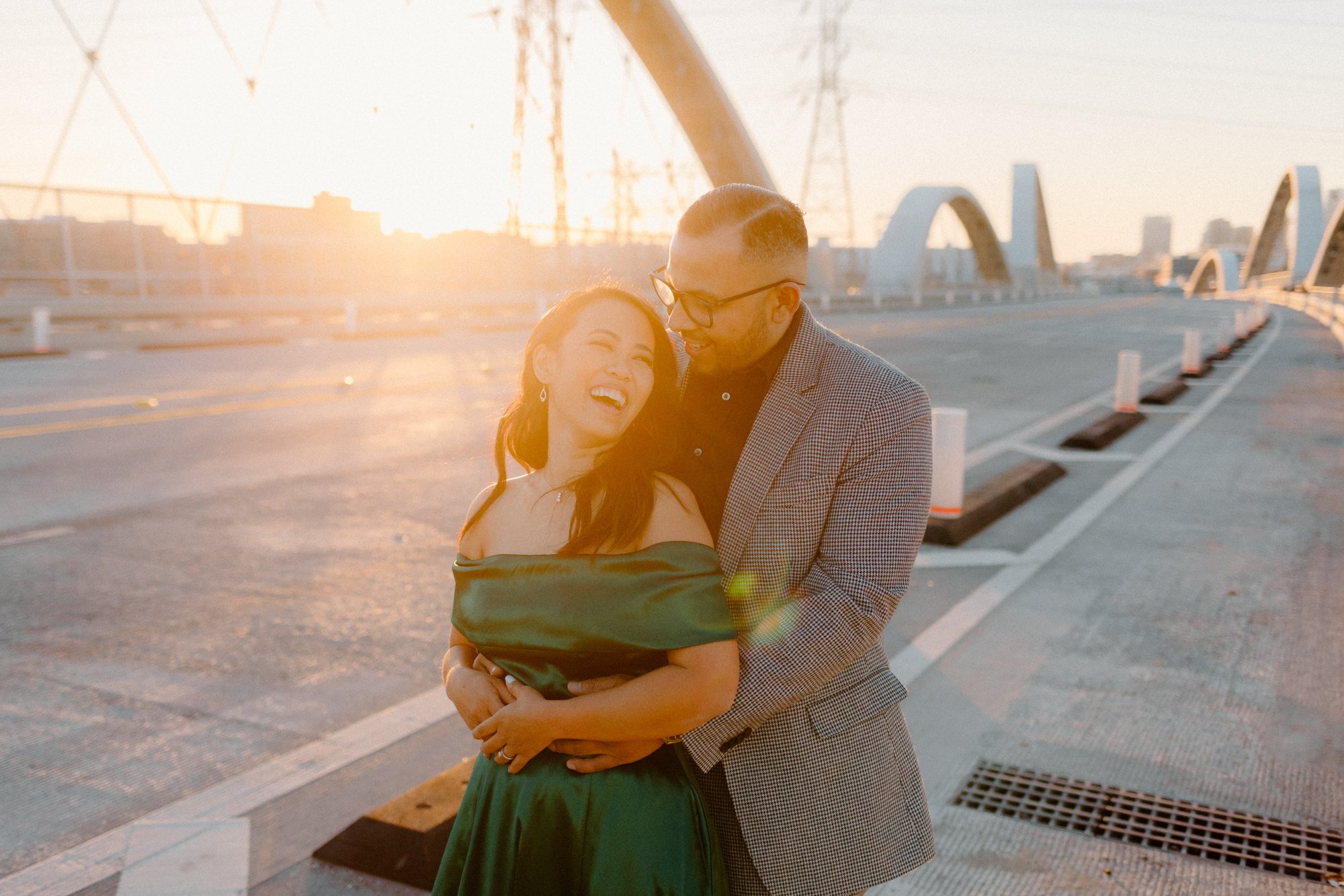 golden hour photo of a couple laughing together on 6th street bridge, candid engagement photography by by evening photo and films, los angeles engagement and wedding photographer
