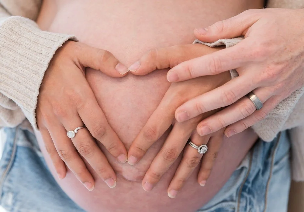 Couple forming a heart shape with their hands over a pregnant bump representing holistic fertility consultations and prenatal care