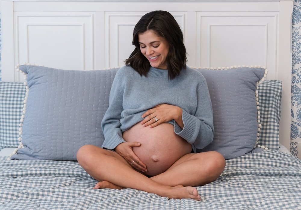Smiling pregnant woman sitting on a bed cradling her belly for pregnancy care at Cache Valley Birth Center in Logan, Utah