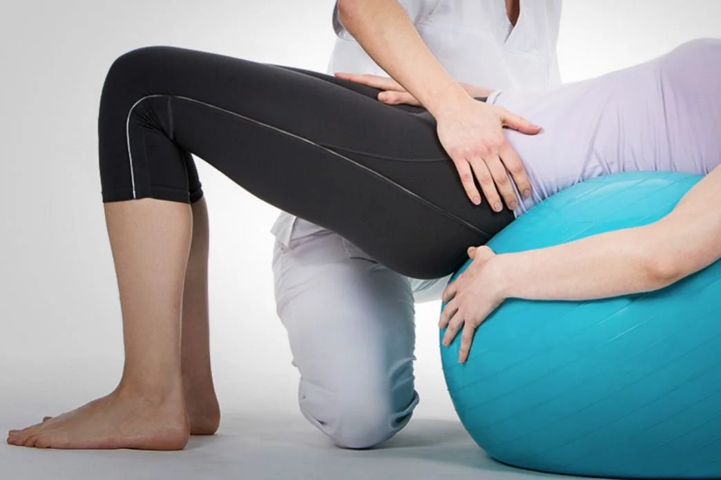 Physical therapist assists a patient with an exercise using a blue stability ball.