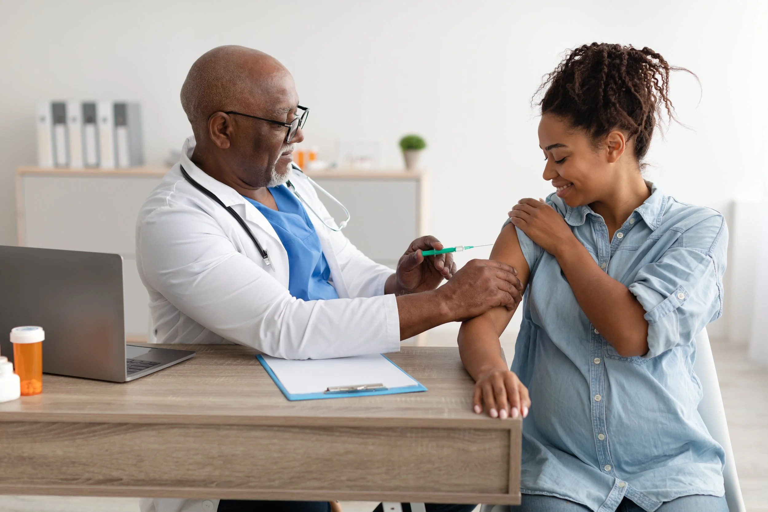 A doctor administering a vaccine to a smiling woman in a medical office.