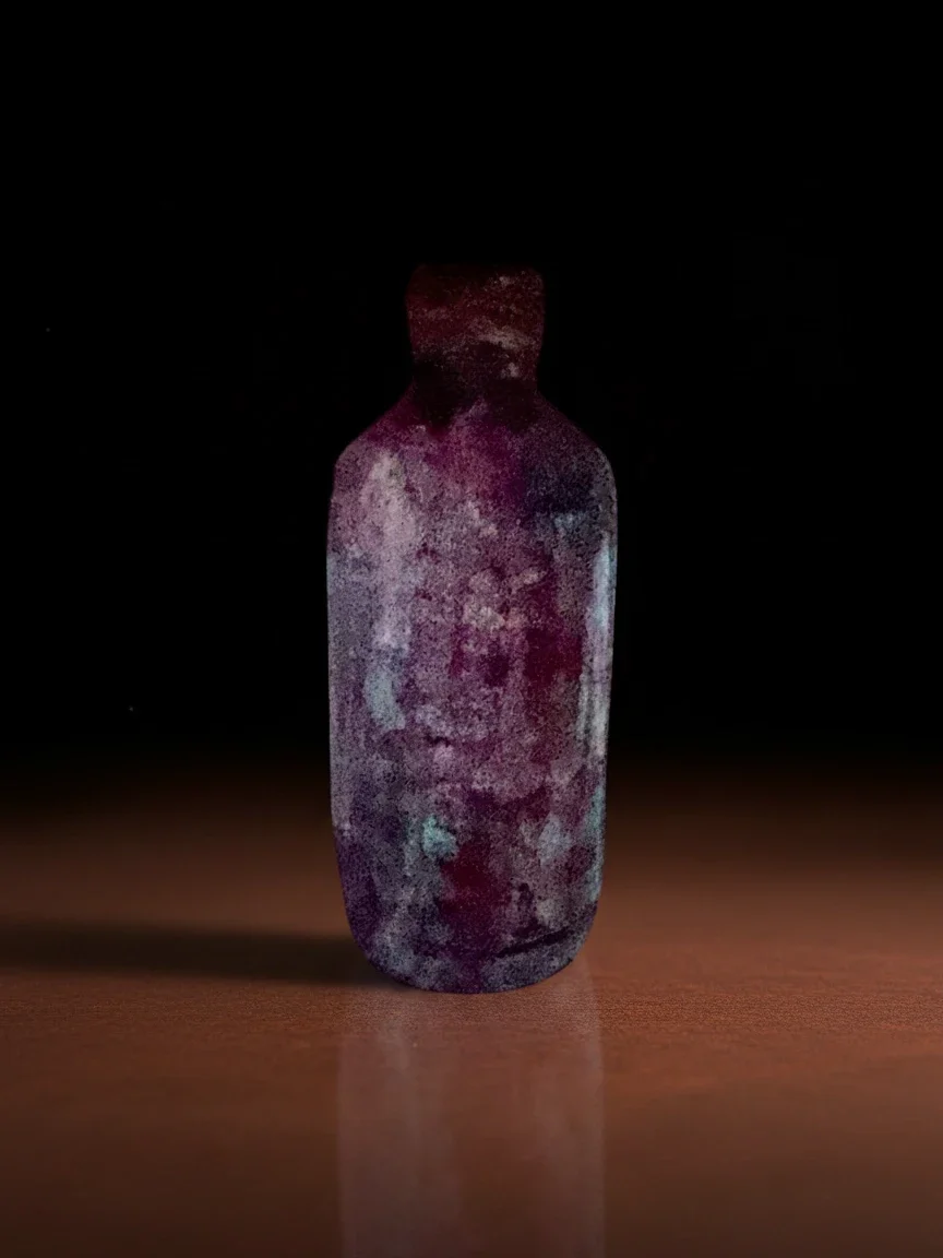 A small glass bottle with a textured, multicolored surface, placed on a wooden surface against a black background.