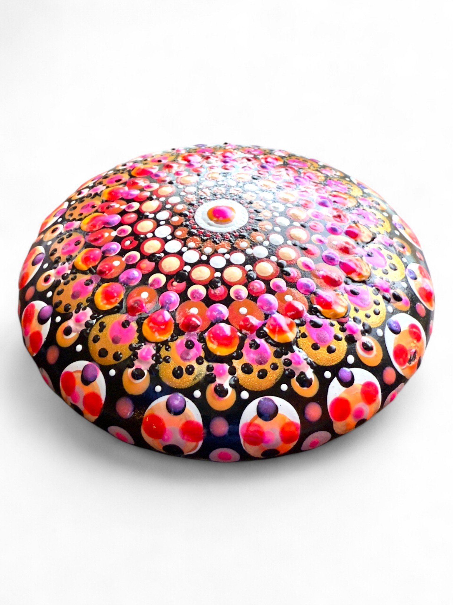 Painted rock with a colorful, dot-patterned design featuring pink, red, purple, black, white, and gold dots on a black background.