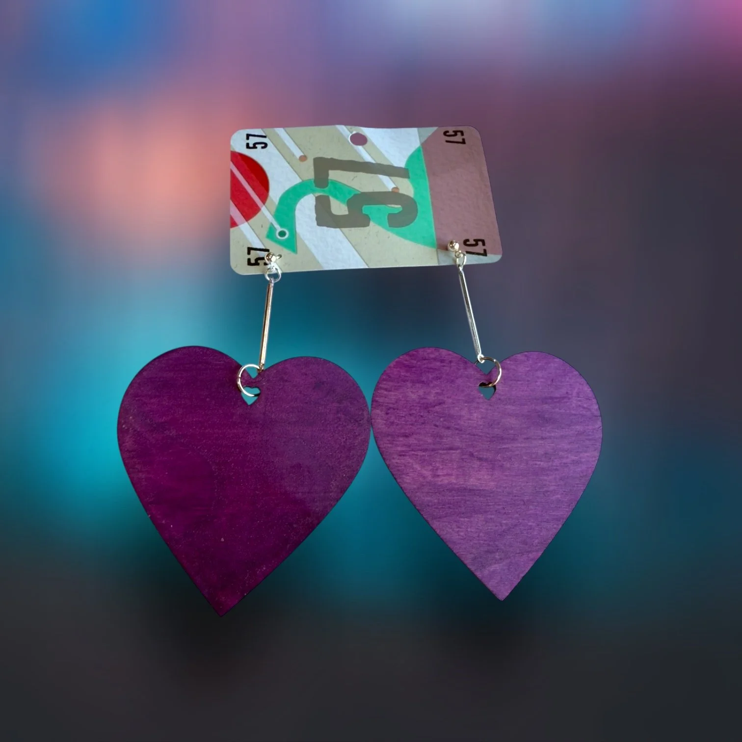 Purple wooden heart earrings hanging from a keychain with transportation signs, including a green arrow and a red circle, on a gradient background.