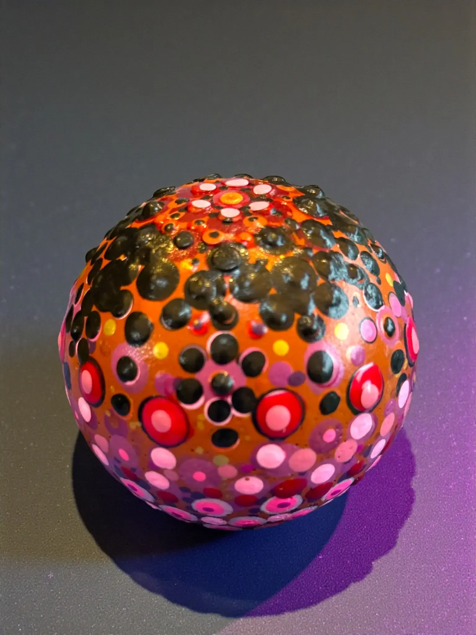 Small globe mandala stone by Color Cult with a terracotta base hue and pink, red, orange, yellow, and black dot mandala artwork.
