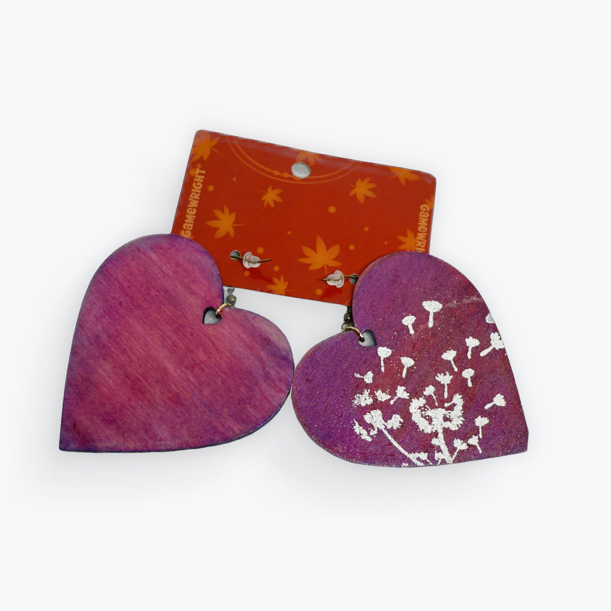 Close-up of painted wooden hearts with purple and pink hues, attached with small metallic eyelets, and an orange label with yellow floral patterns partially visible.