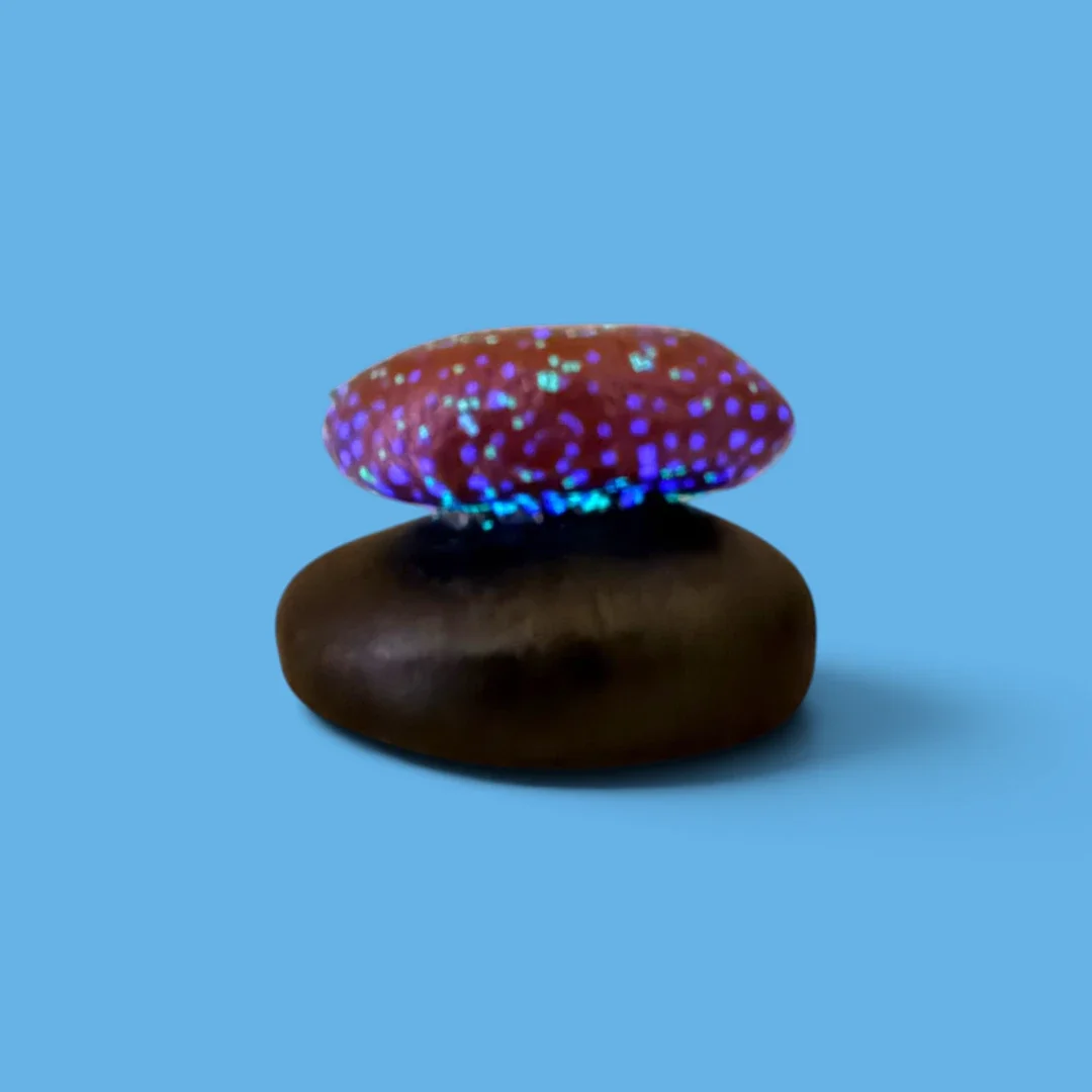 Stacked smooth hand-painted stones with glow-in-the-dark elements on a blue background.