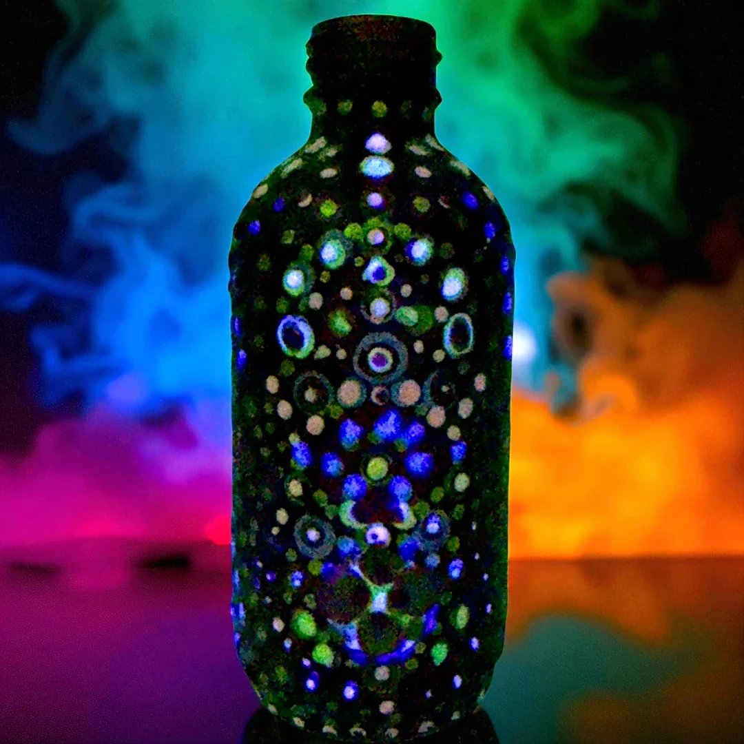 A black bottle with glowing, colorful circular patterns, surrounded by vibrant colored smoke in the background.