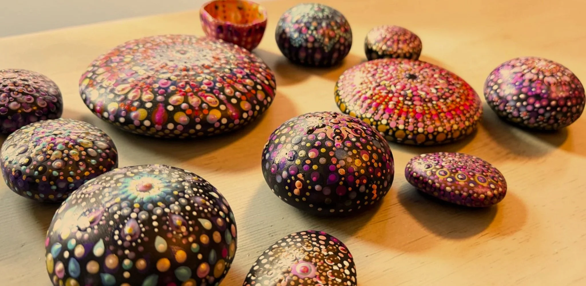 Decorative rocks painted with colorful dot patterns arranged on a wooden surface.