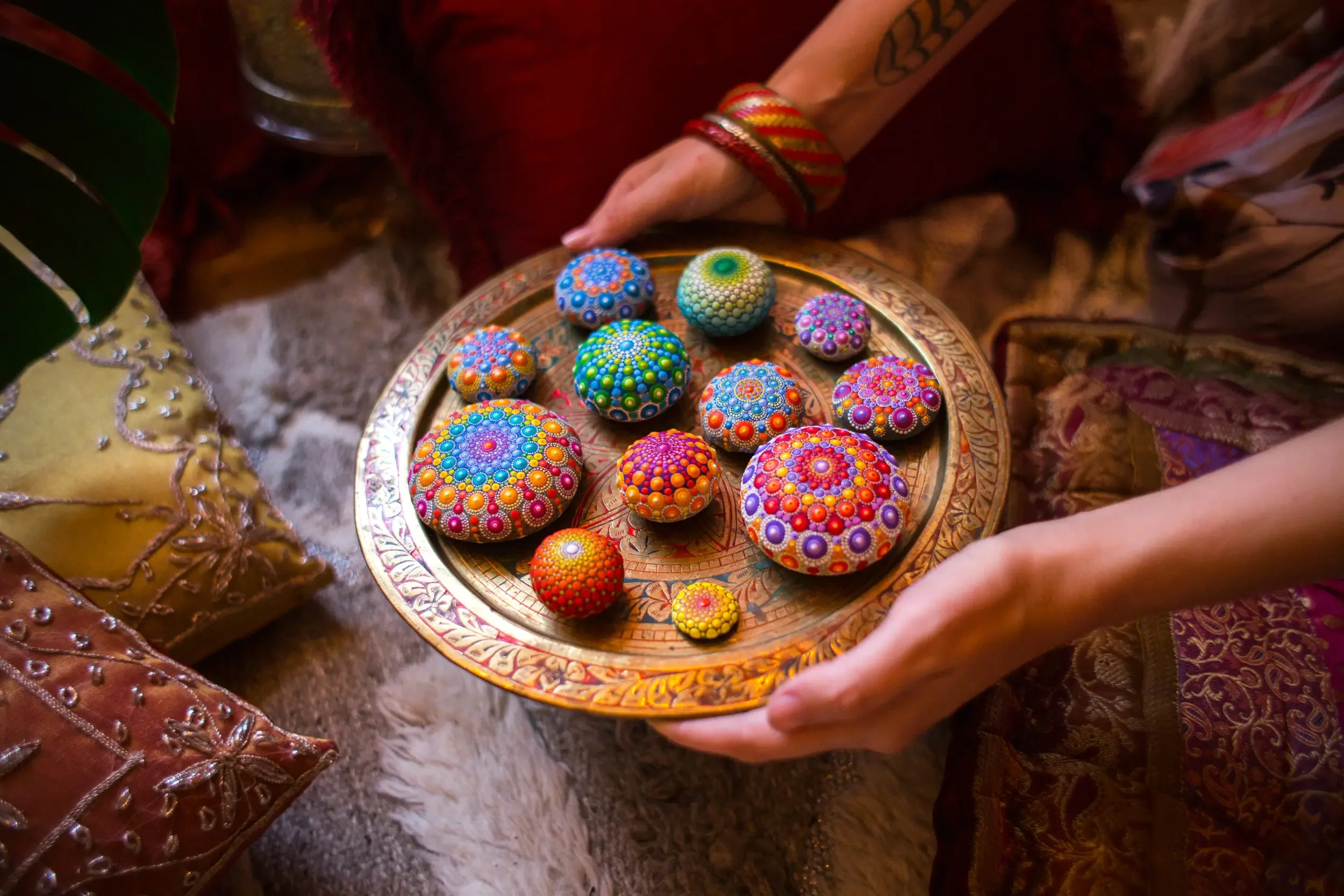 A plated display of mandala stones with colorful dot mandala artwork. The background shows decorative pillows.