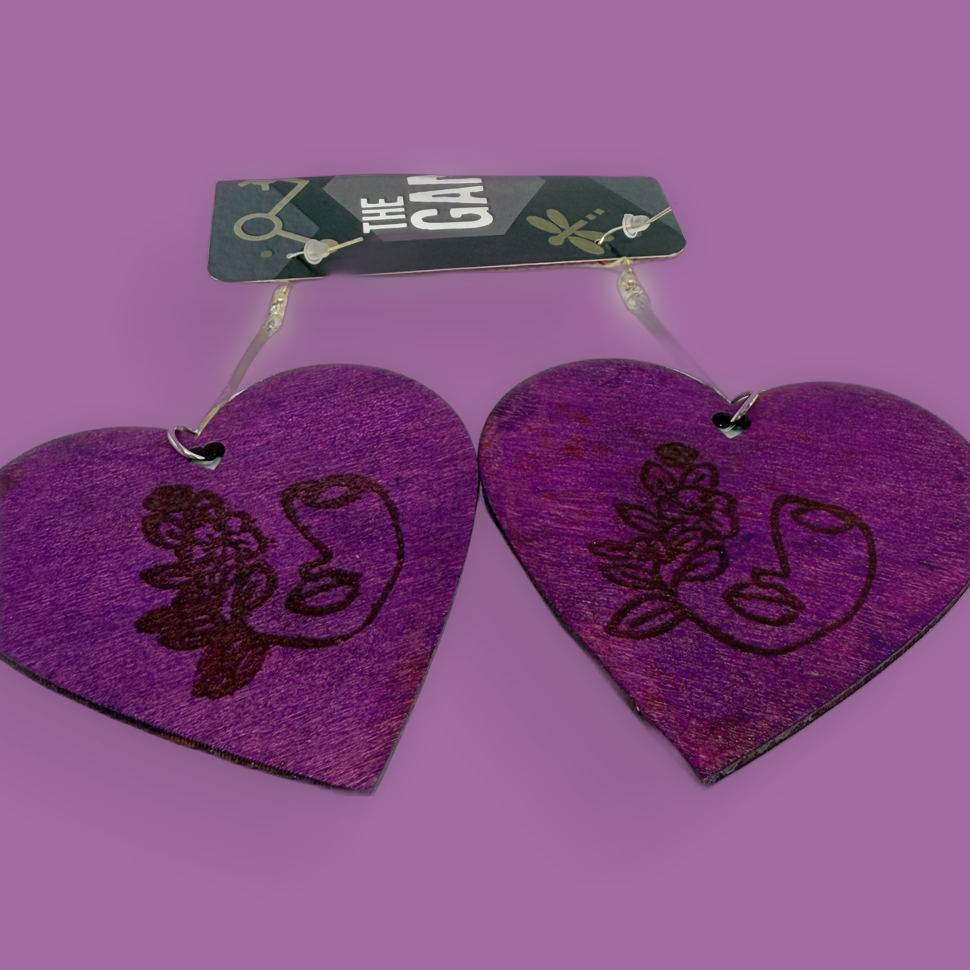Purple heart-shaped earrings with a heat embossed design showing the silhouette of a woman's face on a purple background.