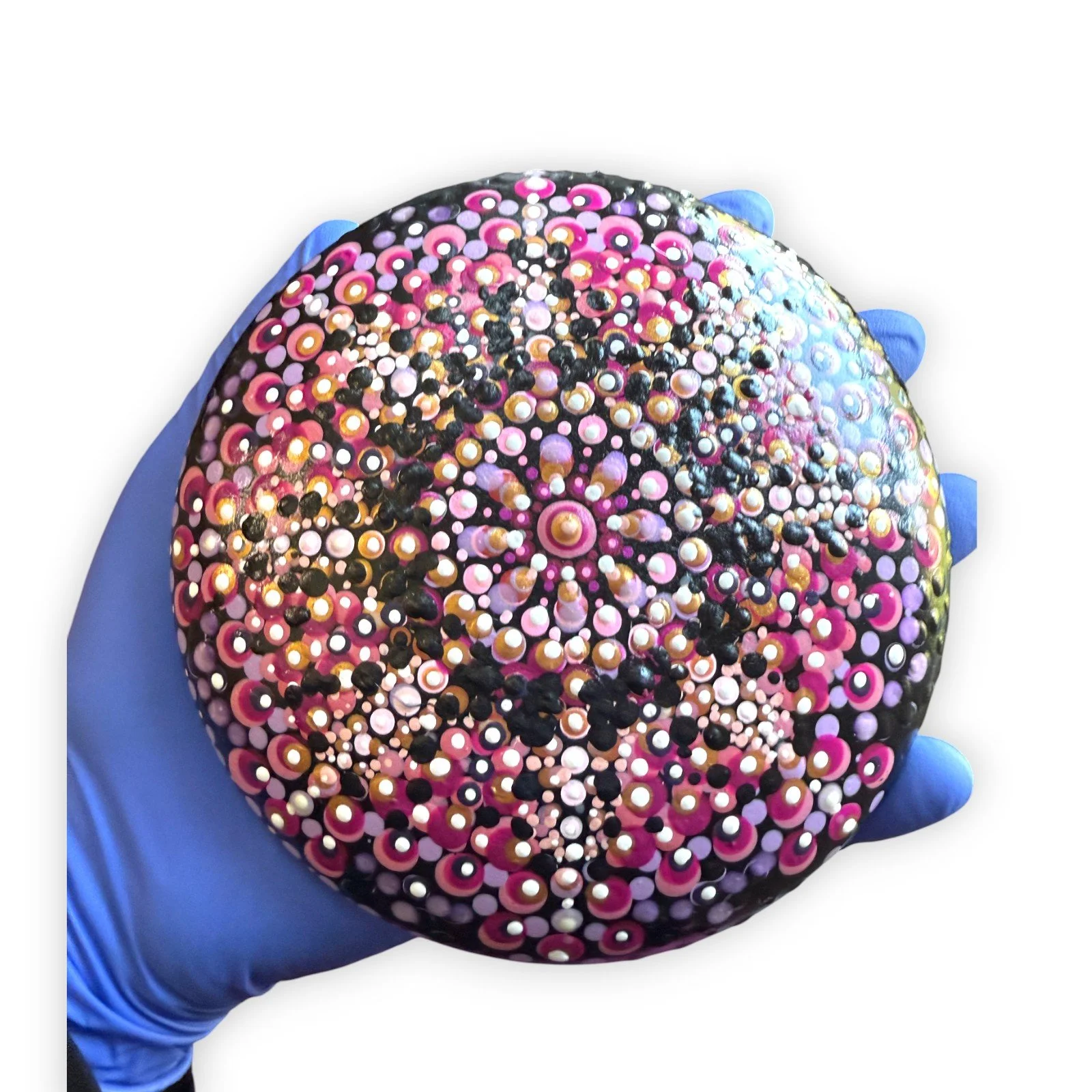A person wearing blue gloves holding a spherical decorative object covered in a pattern of pink, purple, white, and black dot designs.