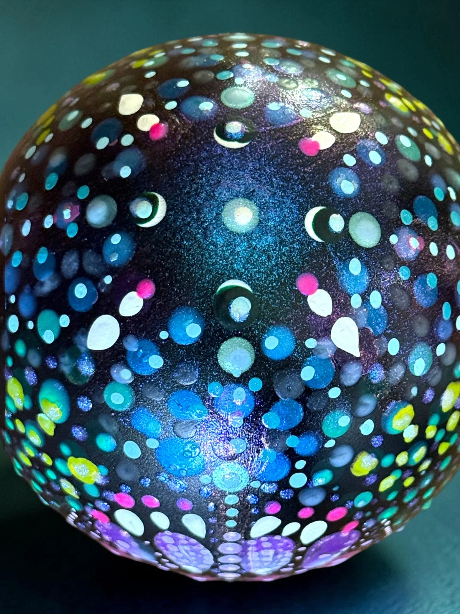 A black spherical object with colorful dots and patterns that resemble a starry night sky or galaxy, made of a painted or decorated material.