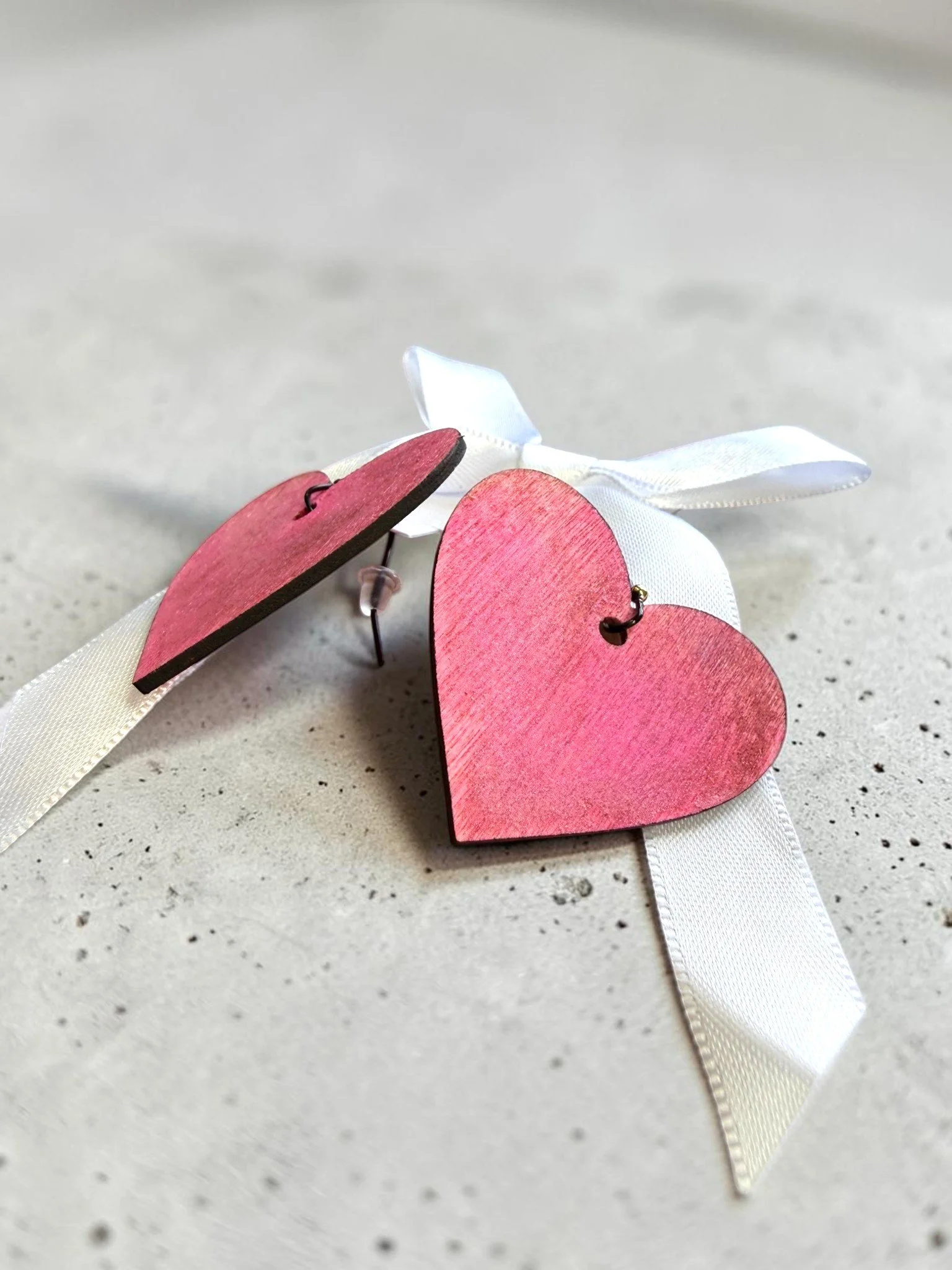 Pink and red wooden heart-shaped cutouts tied with a white ribbon on a speckled gray surface.