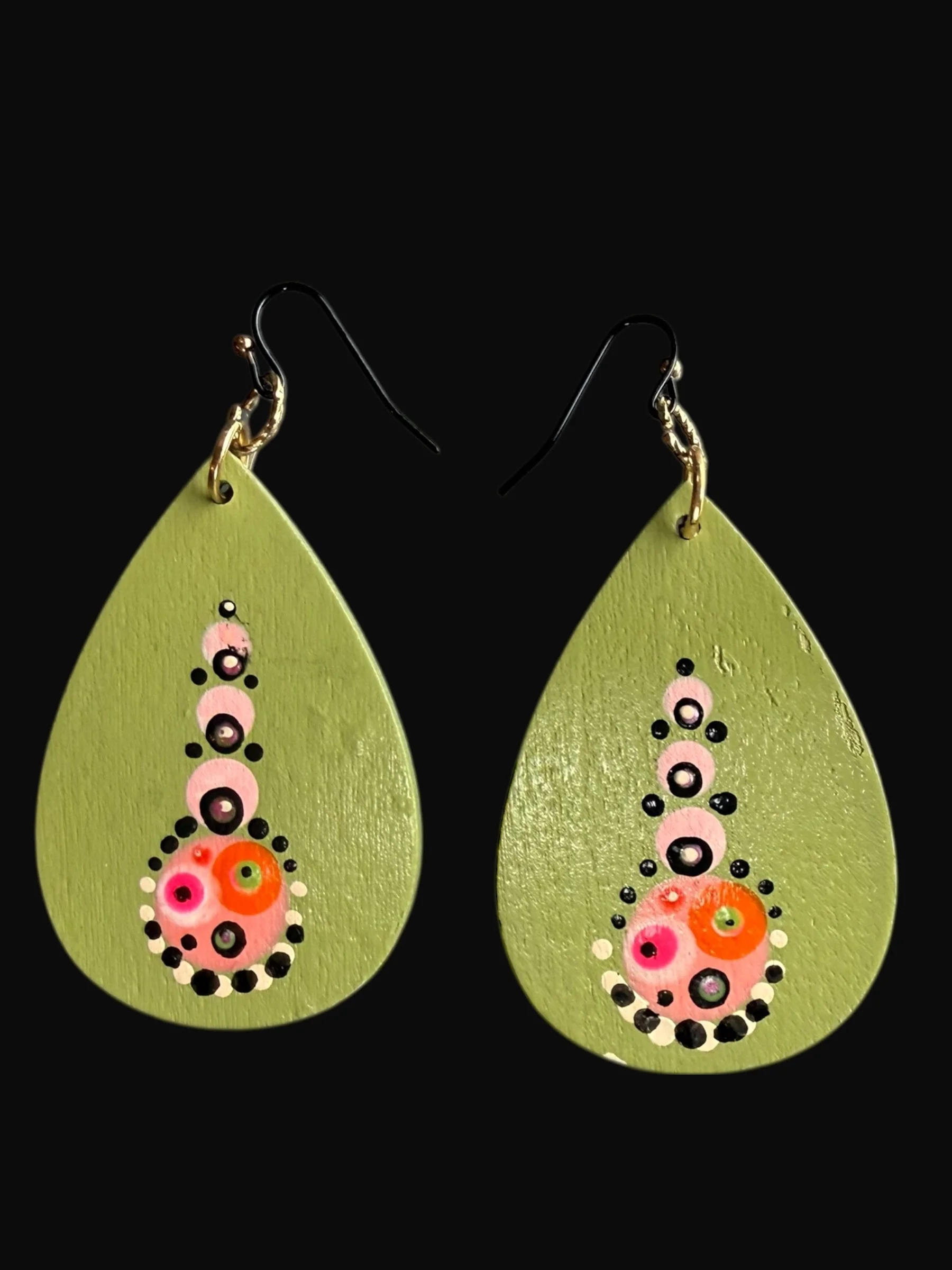 Pair of green teardrop-shaped earrings with black, pink, white, and orange circular and dotted decorative patterns against a black background.
