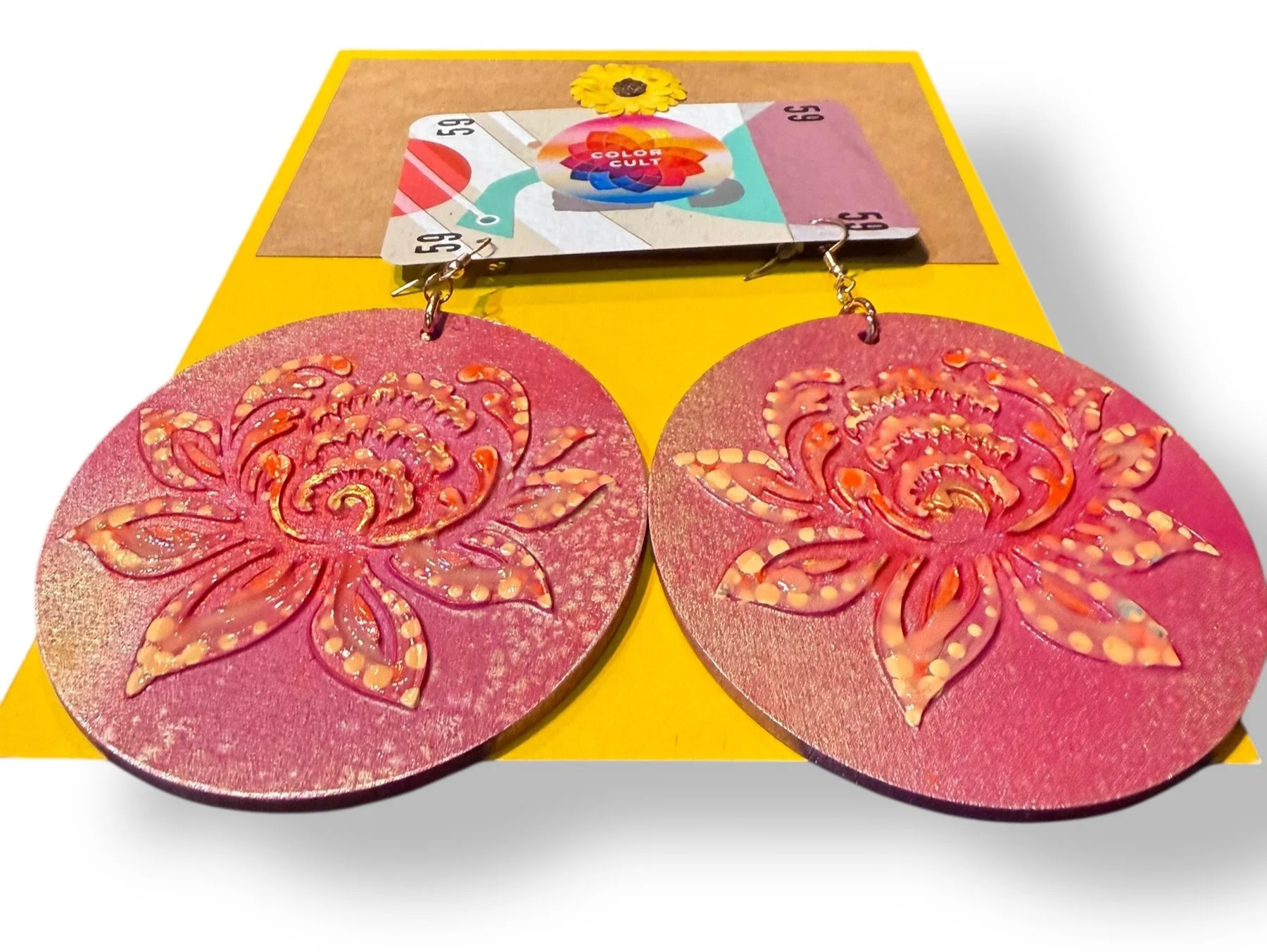 Pair of large pink earrings with intricate floral design on yellow packaging.