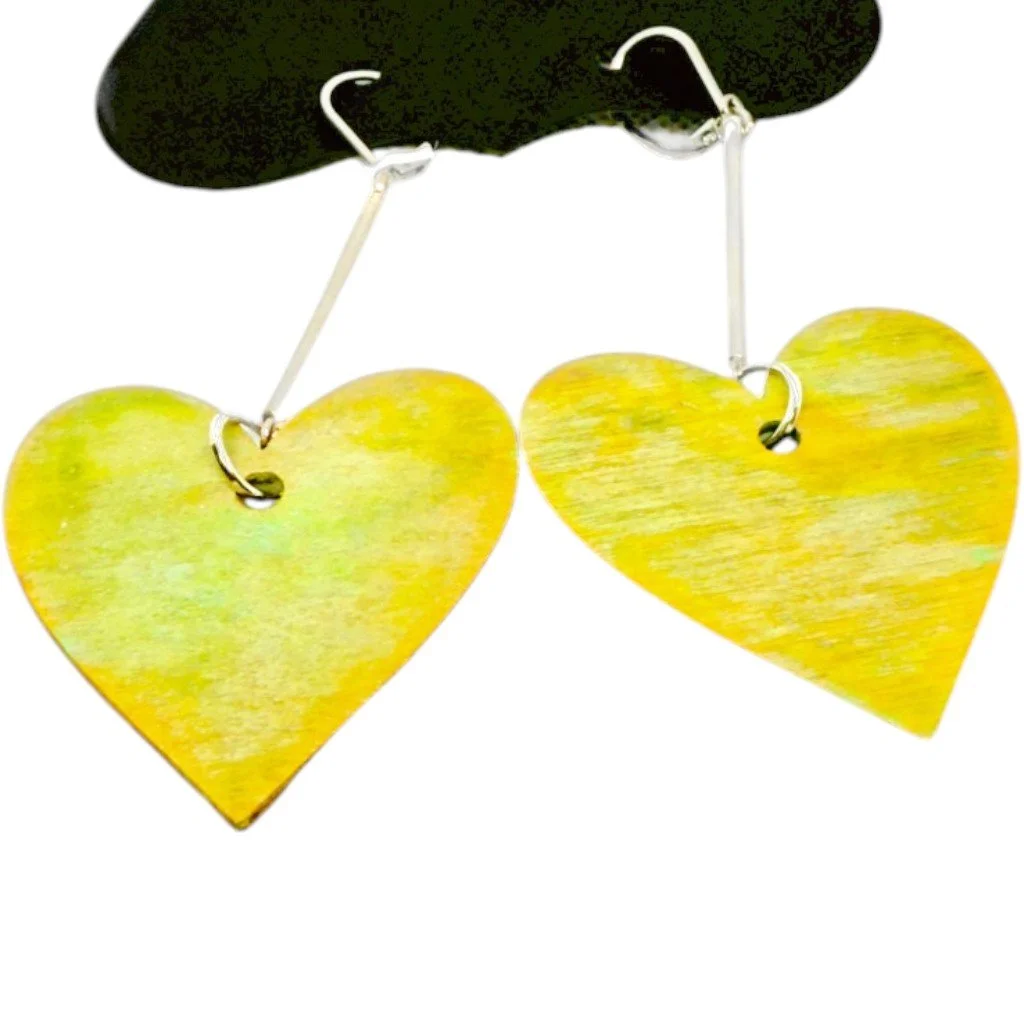 Pair of earrings with yellow heart-shaped wooden pendants hanging from silver hooks, mounted on a black display stand.