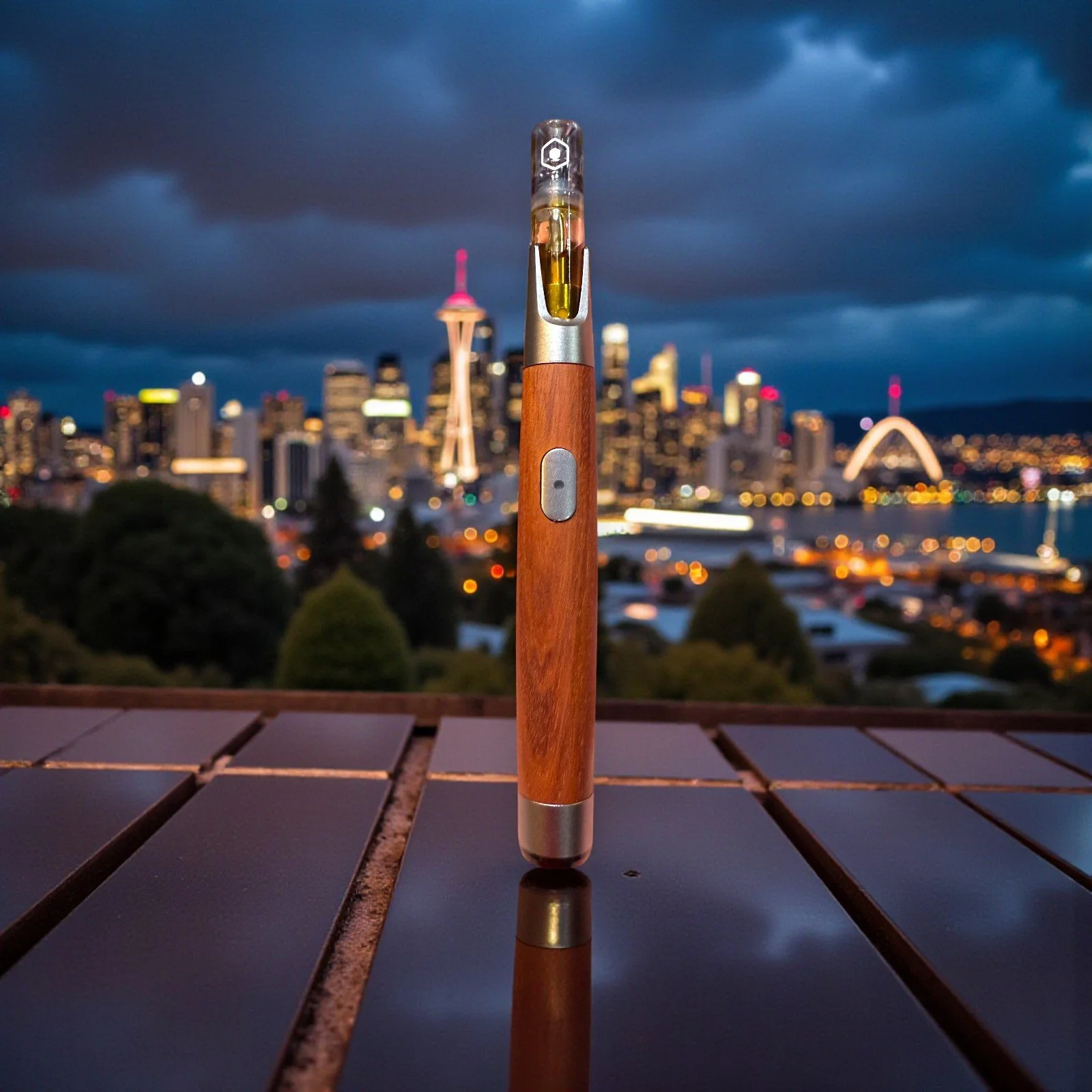 A vaporizer pen with a wooden body standing on a wooden table outdoors at dusk with a city skyline in the background.