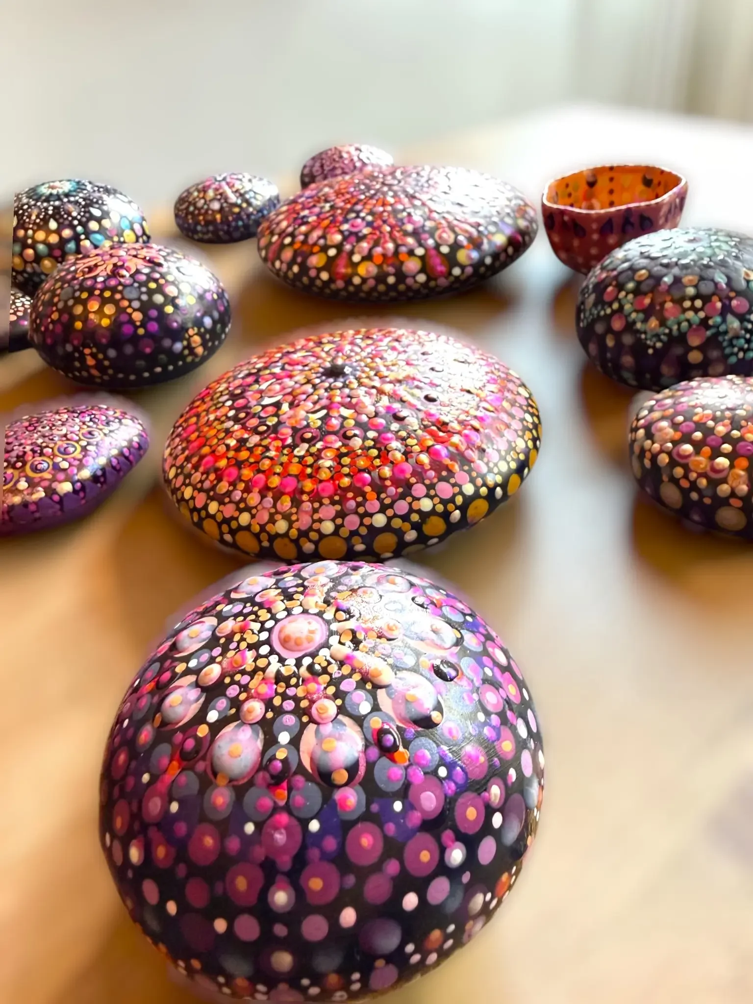 Colorful mandala stones made by Color Cult arranged on a table. The stones all have intricate dot mandala artwork in many colors and designs.