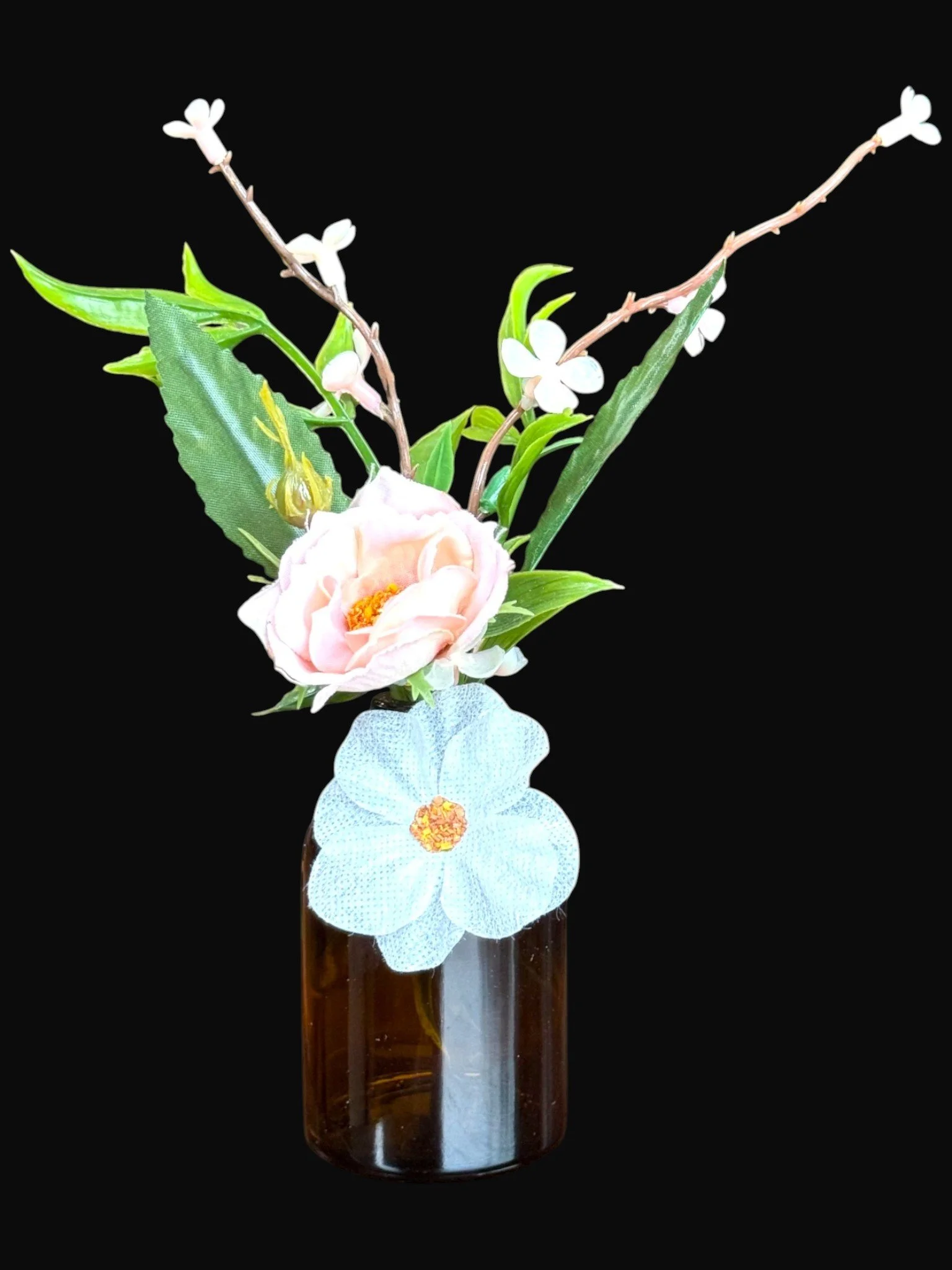 Artificial flower arrangement in a brown glass vase with pink and white flowers and green leaves against a black background.