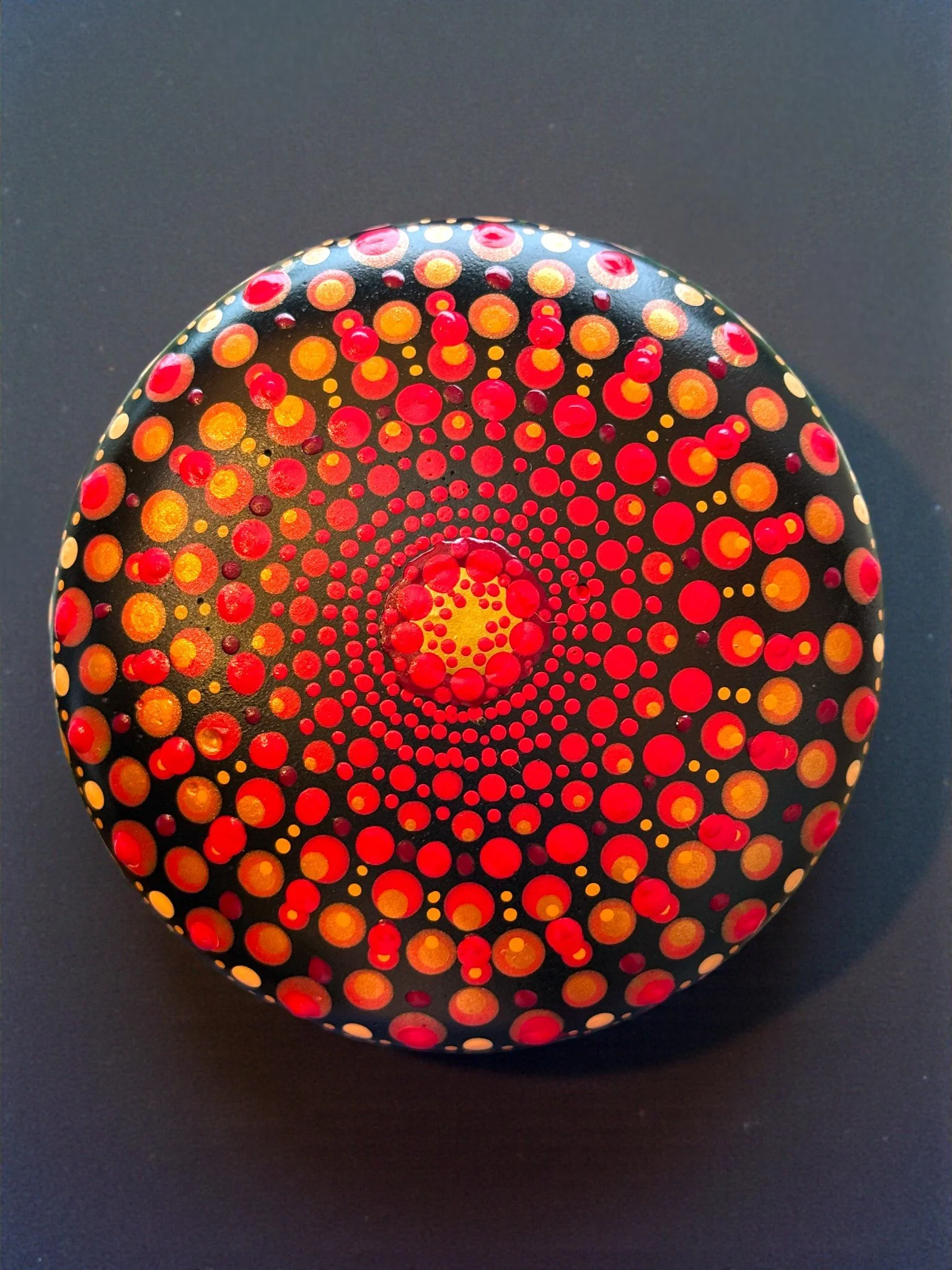 Painted rock with circular dot patterns in red, yellow, and orange on a black background.