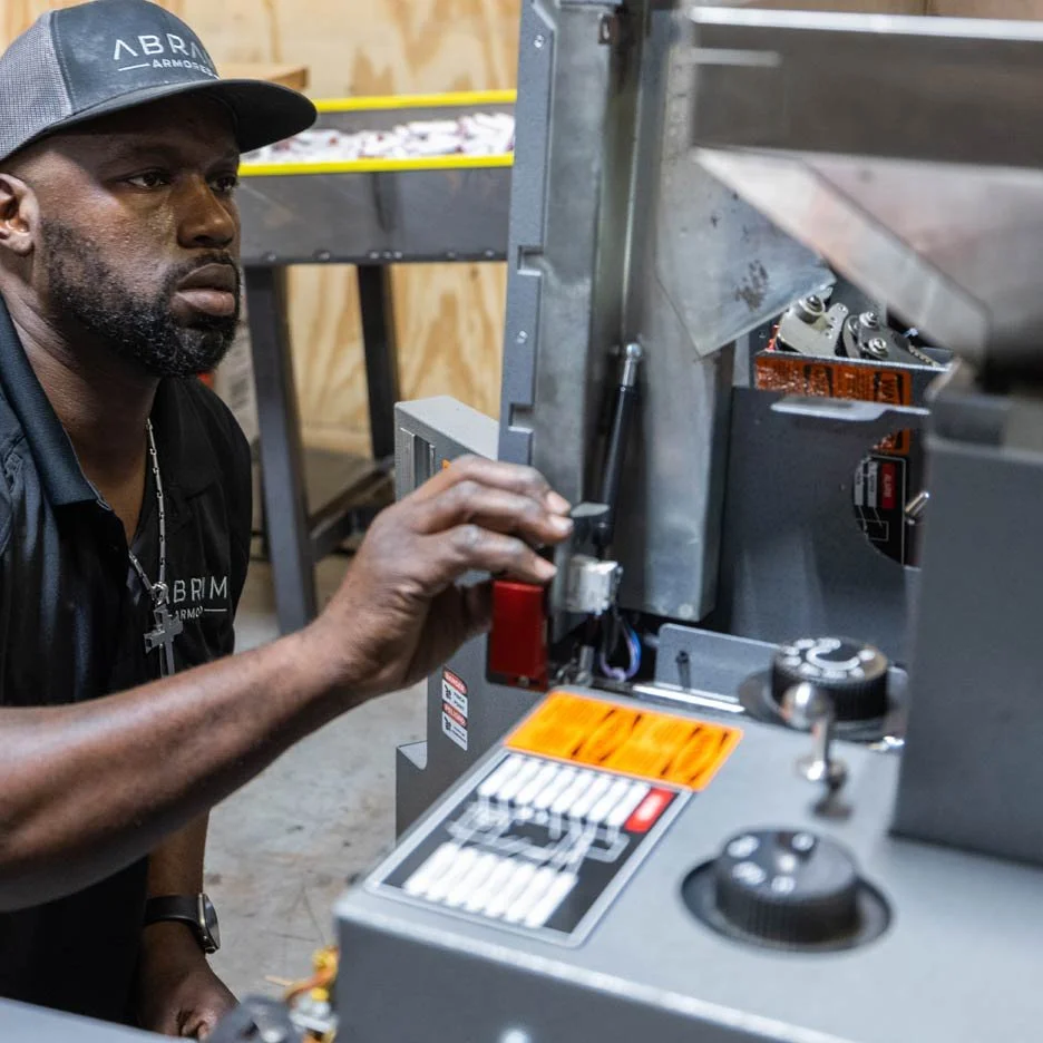 Person operating machinery in a workshop, wearing a hat and black shirt.