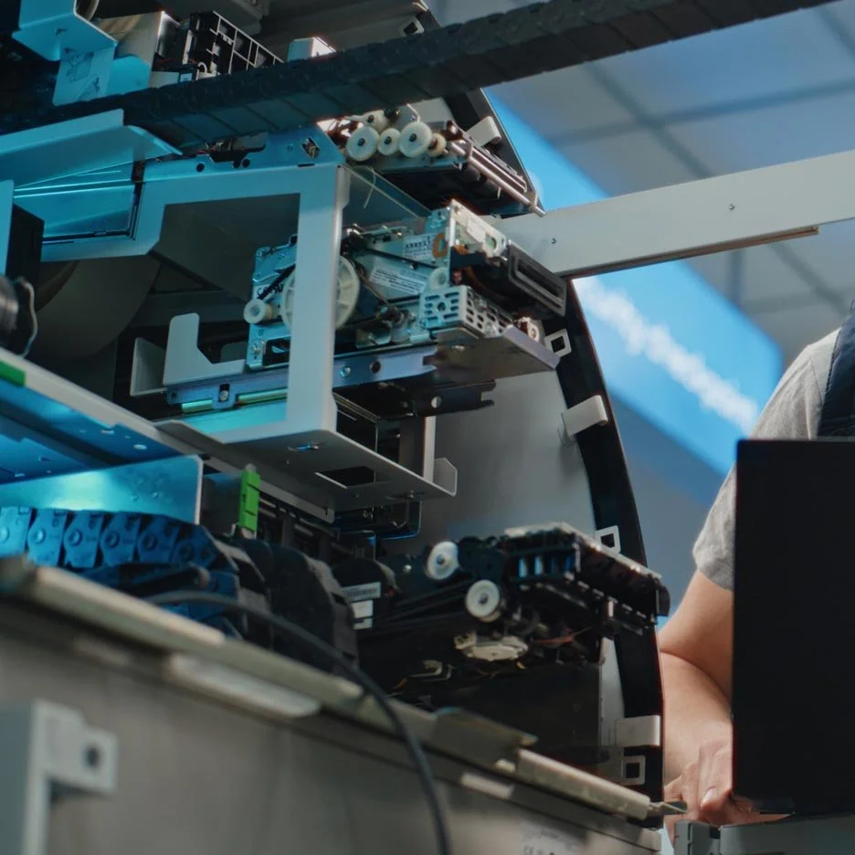 A man operating industrial equipment, wearing a cap and work shirt, adjusting controls on a machine in a workshop setting.