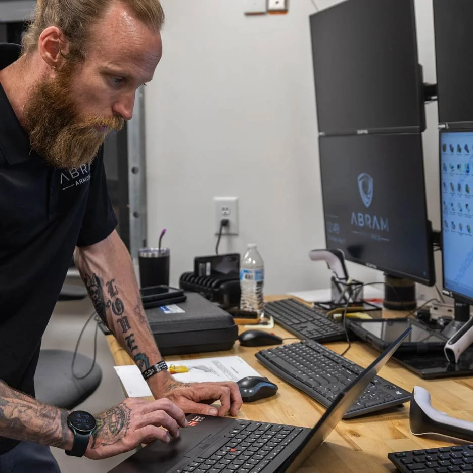 Man using a laptop in an office with dual monitors, a water bottle, and various office supplies on a desk.
