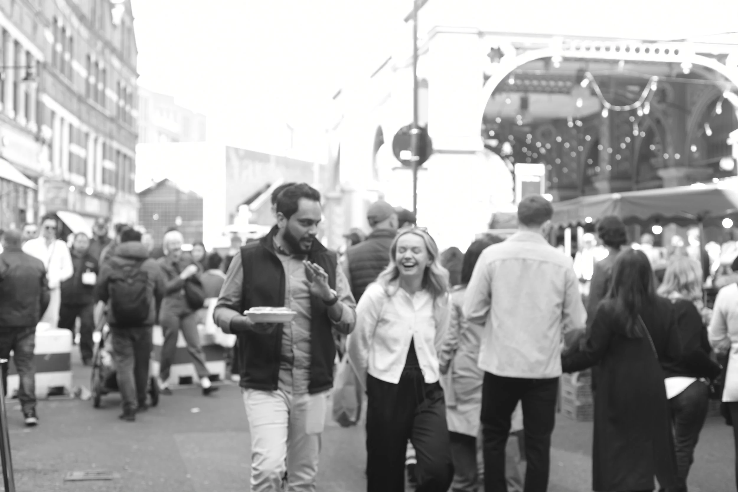 People walking and socializing at an outdoor market or street fair with booths and lights.