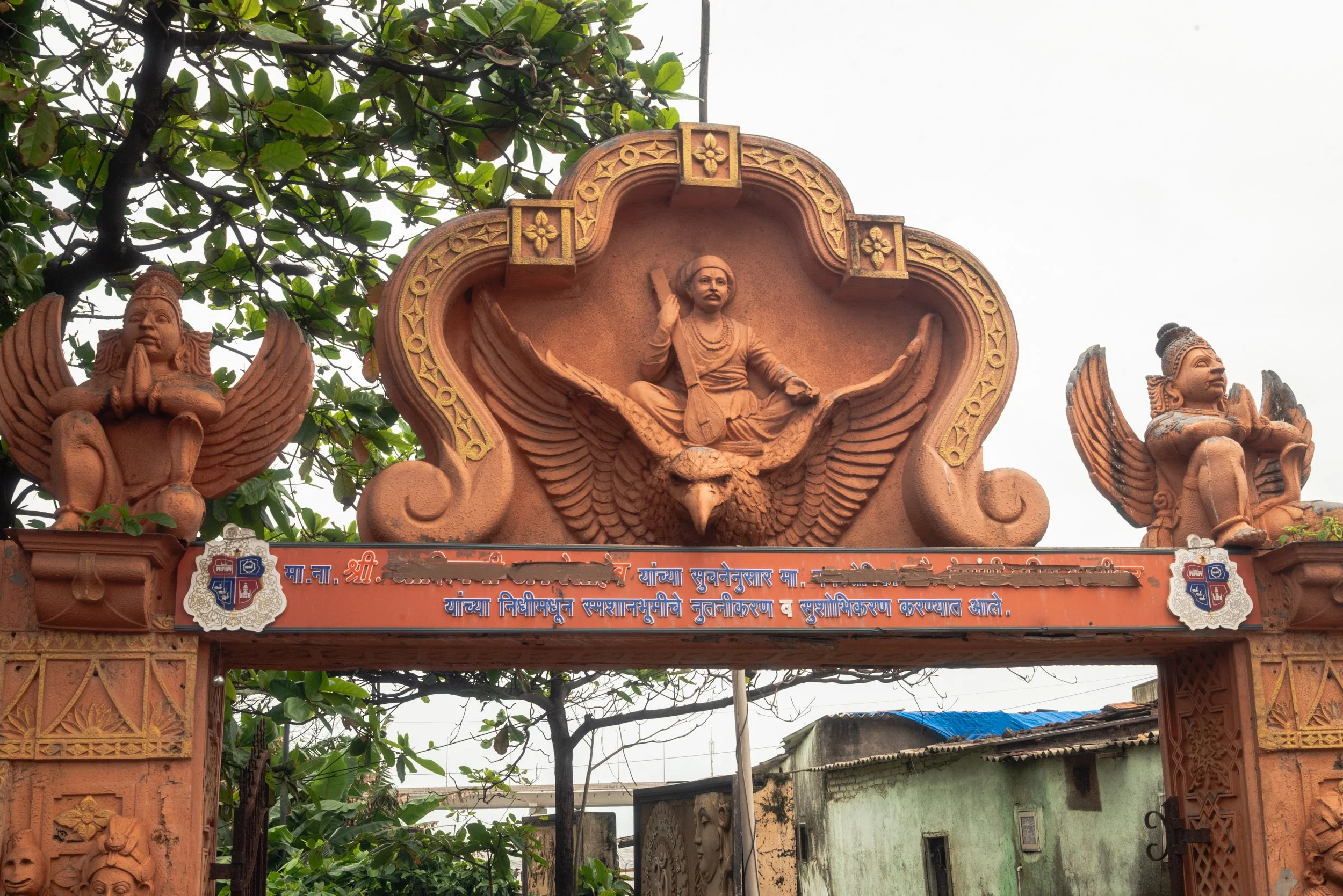 Decorative entrance arch with sculptures, including a central figure on a flying eagle, flanked by exterior figures, with a sign in a regional language.