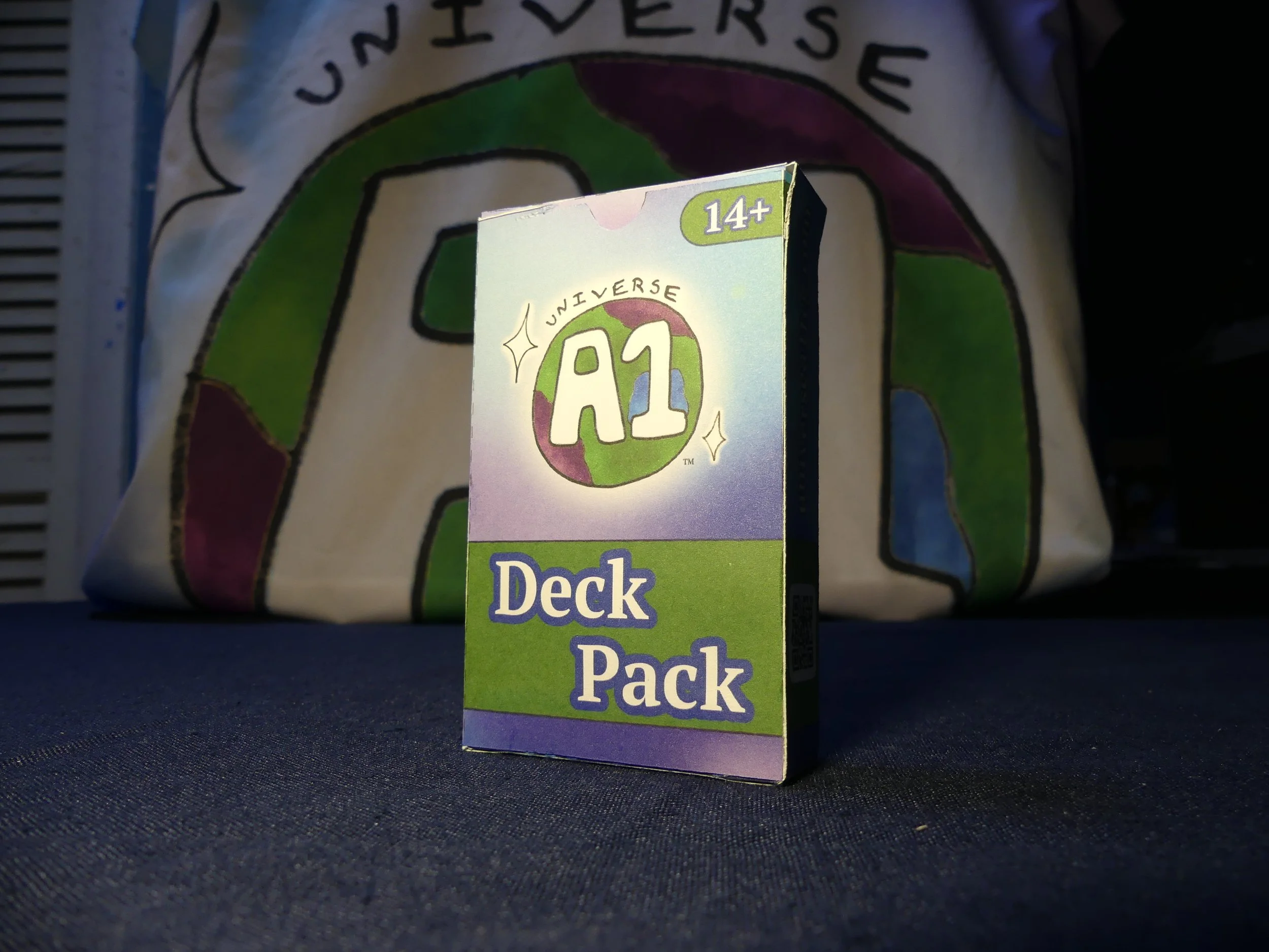 A small box labeled 'Deck Pack' with the 'Universe A1' logo on it, standing on a dark surface with a colorful illustrated  background.